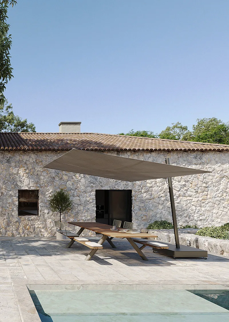 Panigiri picknicktafel met een grote gekantelde Sensu-schaduw op een stenen terras naast een ondiep zwembad, gelegen tegen een mediterrane stenen villa.