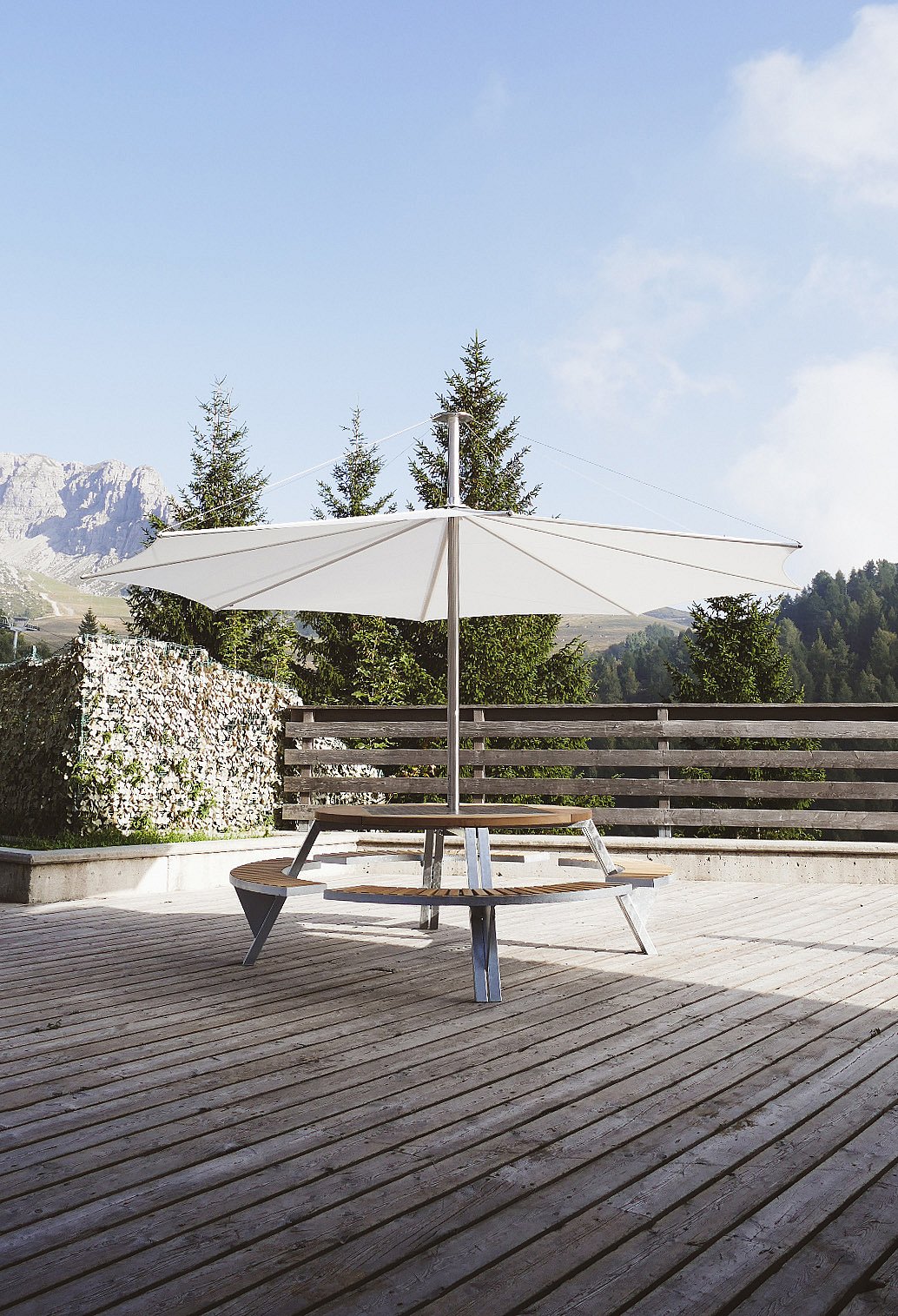 Sunny mountain terrace with wooden picnic tables overlooking a green alpine landscape and distant peaks