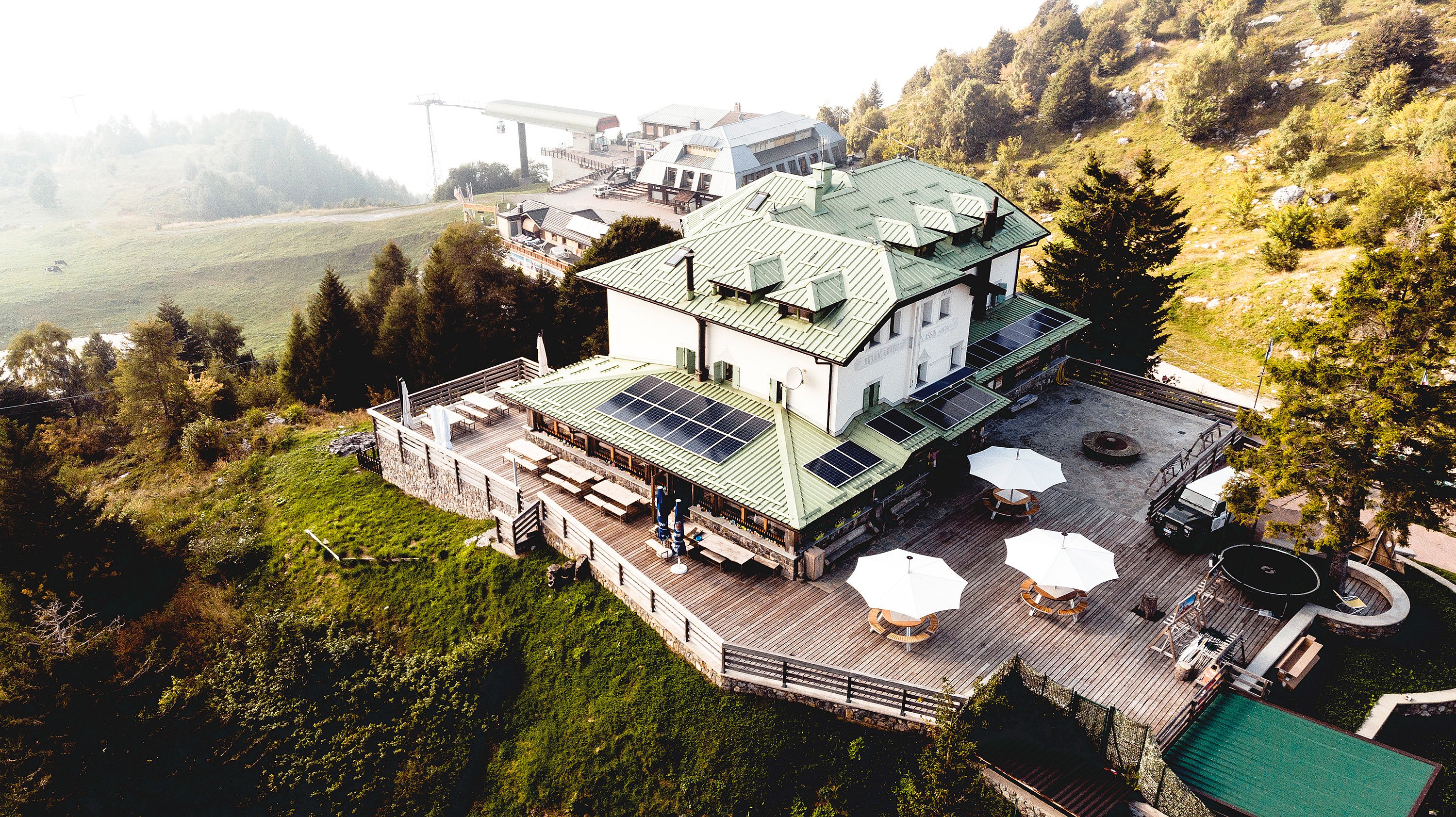 Chalet de montagne avec terrasse extérieure meublée avec des tables de pique-nique en bois, situé dans un décor alpin pittoresque.