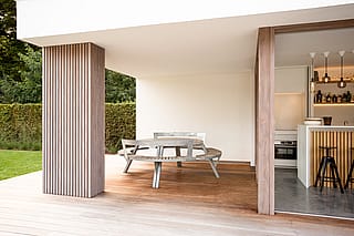Covered terrace with a round gargantua table and circular bench seats next to an open poolhouse kitchen with a bar and black stools.
