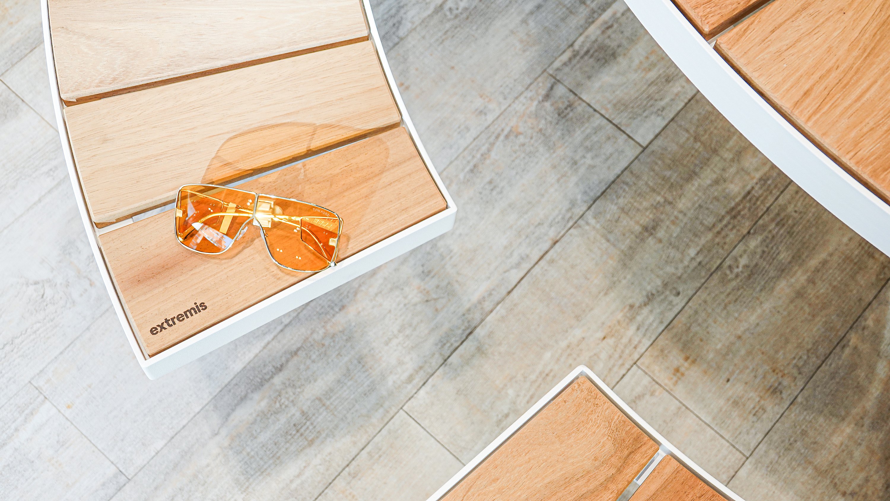 Close-up van oranje getinte pilotenzonnebrillen die rusten op een houten pantagruelbank naast een rond houten tafelblad.