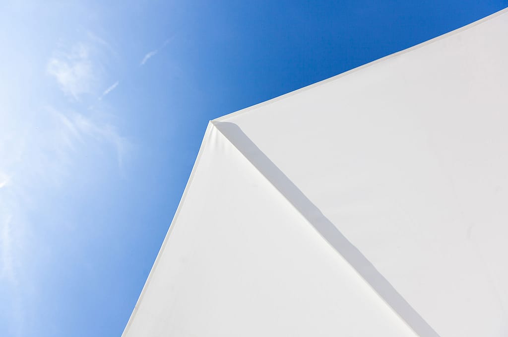 Close-up van de puntige hoek van een witte parasolluifel tegen een felblauwe lucht.