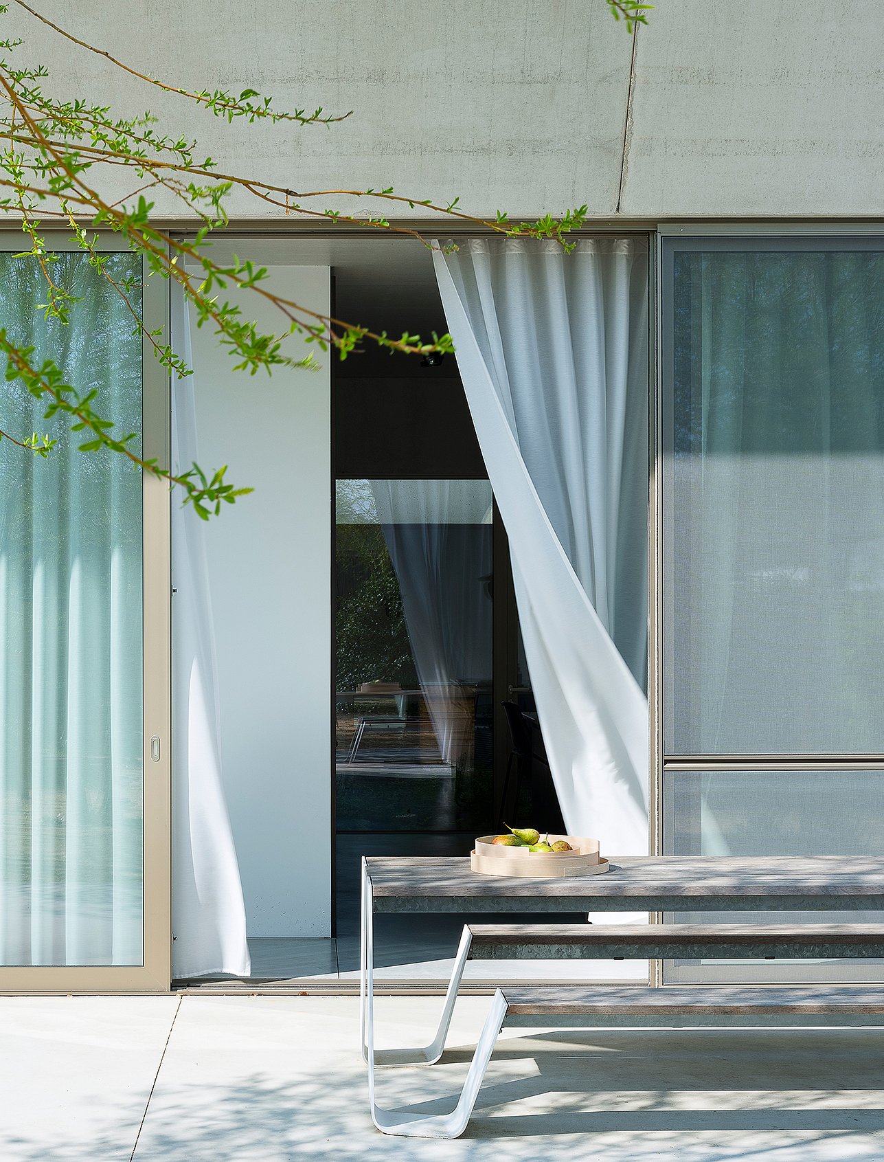 Close view of a white hopper picnic table outside large sliding glass doors, with sheer white curtains blowing inward and a shallow tray on the tabletop.