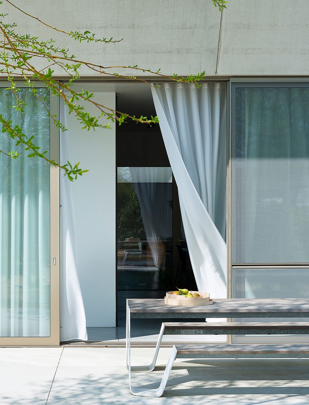 Close view of a white hopper picnic table outside large sliding glass doors, with sheer white curtains blowing inward and a shallow tray on the tabletop.