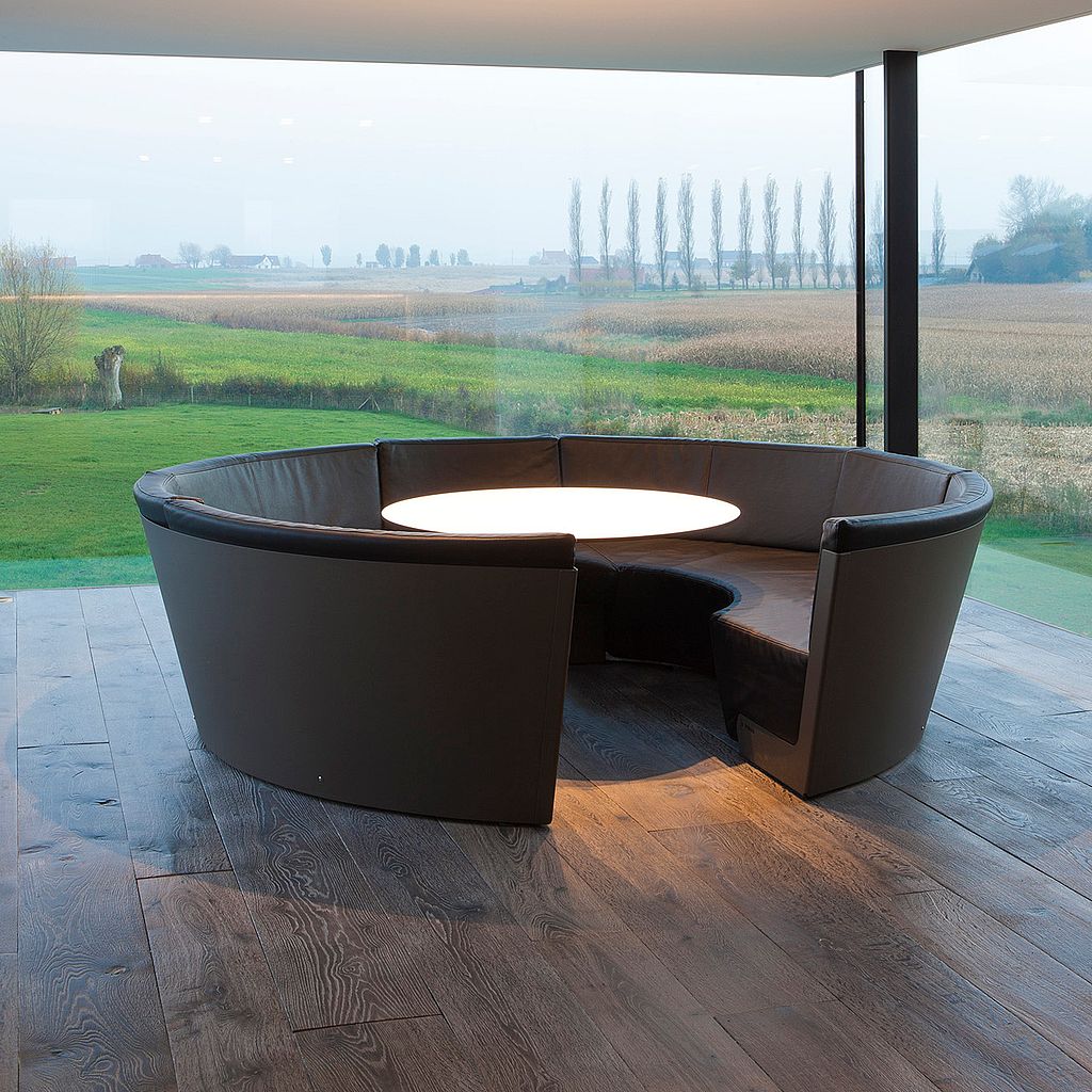 Ein dunkelbrauner Kosmos-Loungesitz mit rundem beleuchteten Tisch auf einer überdachten Terrasse mit Blick auf offene Felder.
