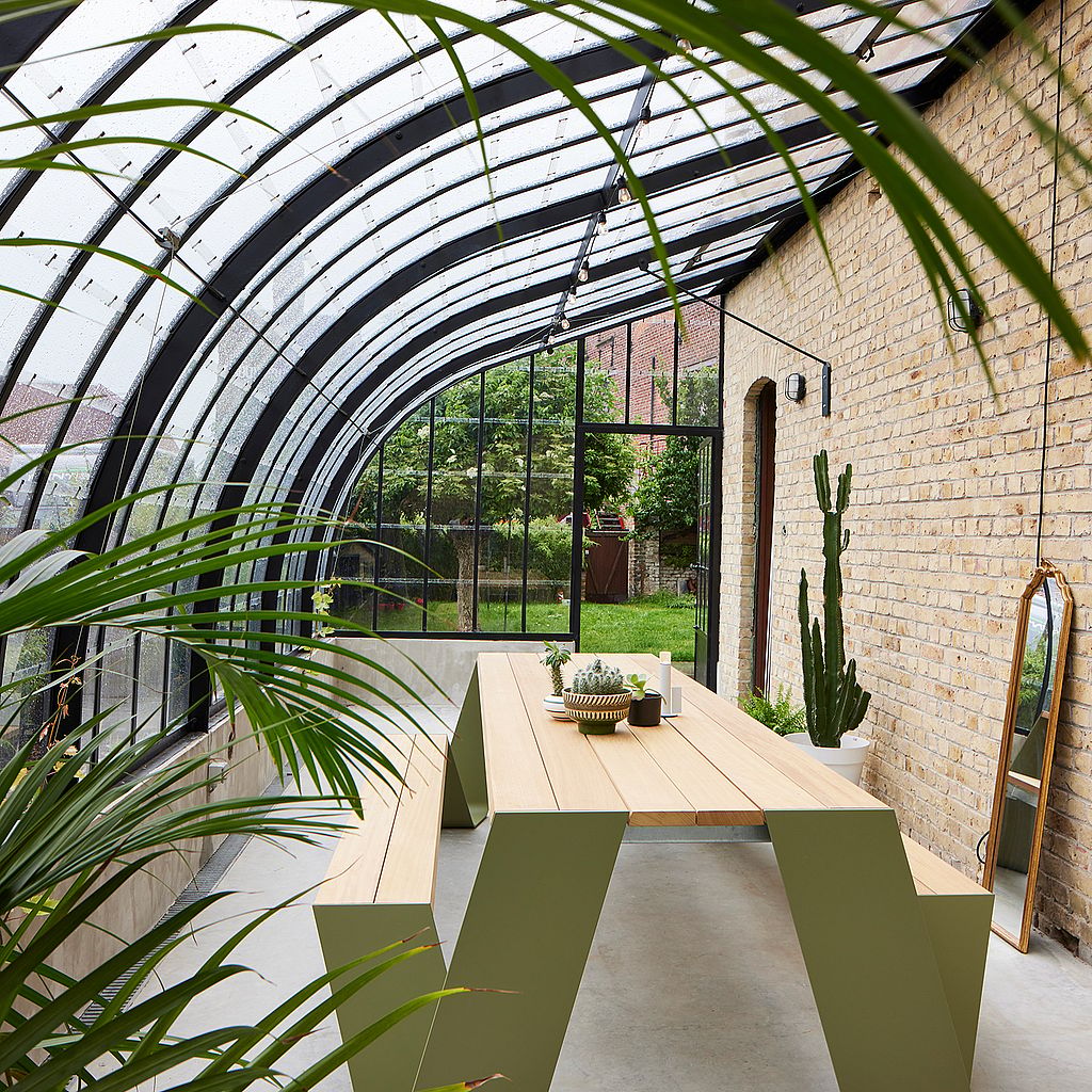 Une table de pique-nique Hopper en bois verte dans une véranda vitrée avec des plantes tropicales.