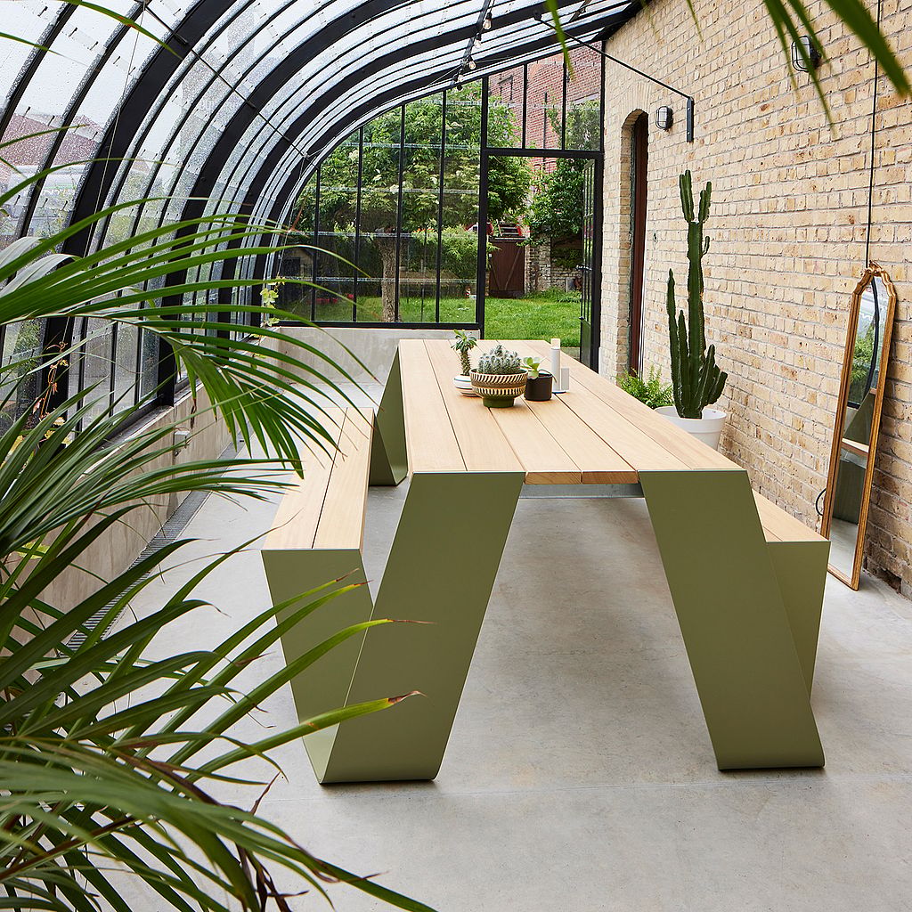A green Hopper wood picnic table in a glass-roofed conservatory with tropical plants.