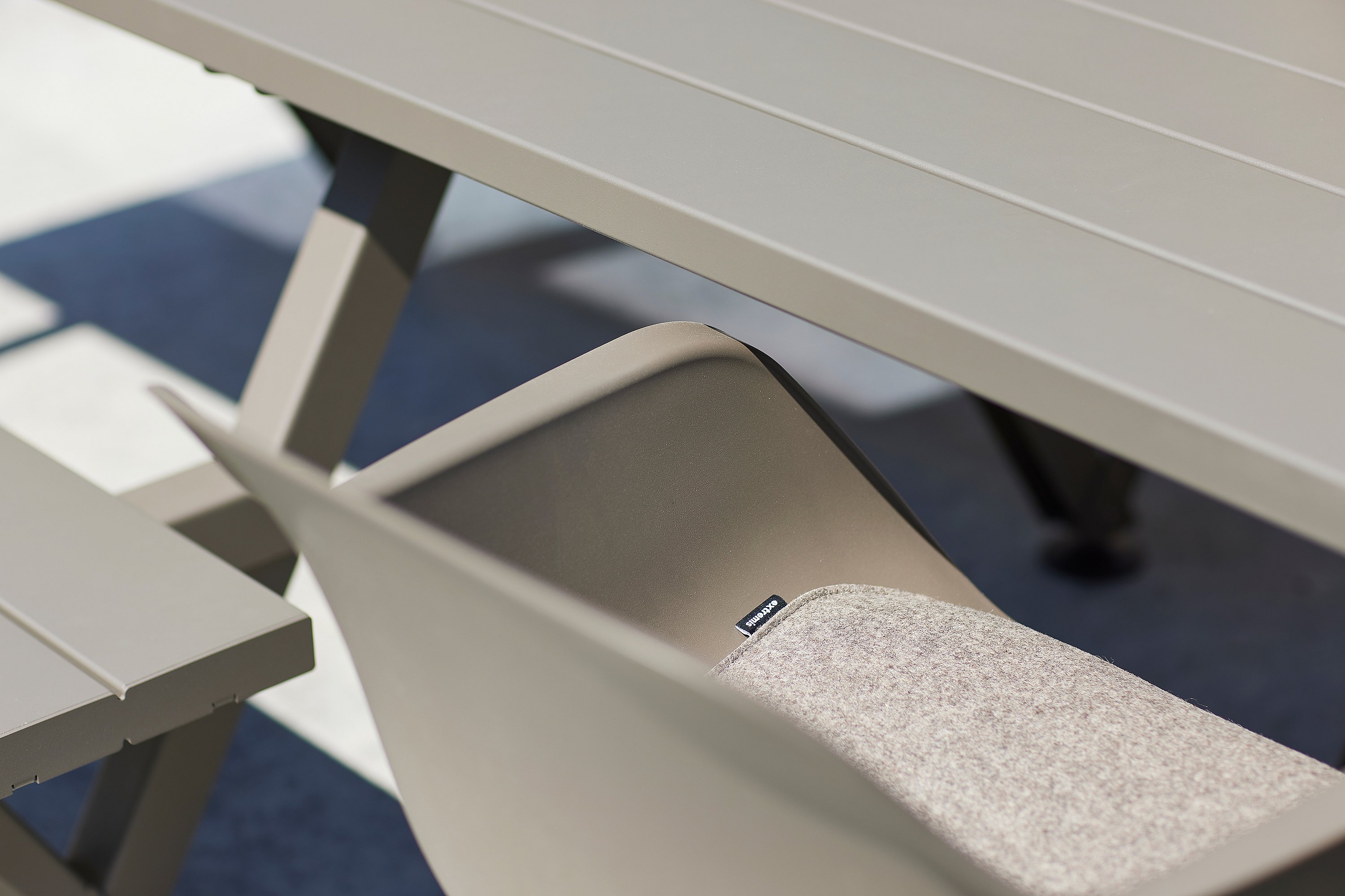 Close-up of a grey outdoor Captain's chair with a light seat cushion tucked under a matching outdoor Marina table and bench.
