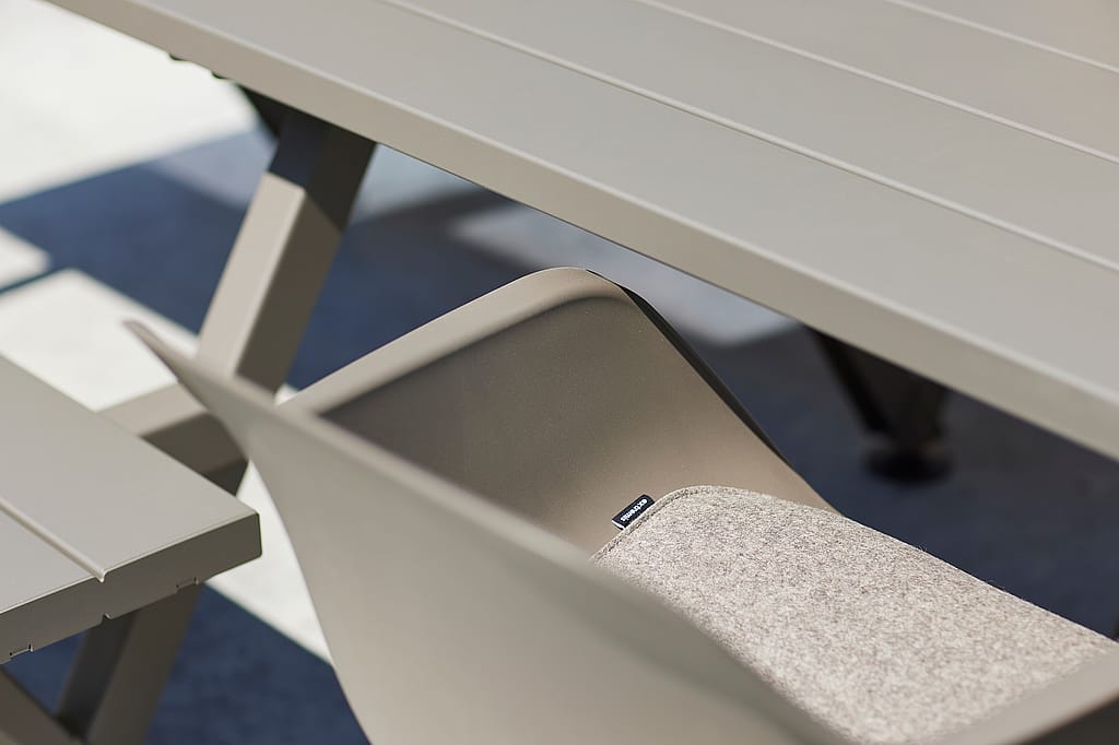 Close-up of a grey outdoor Captain's chair with a light seat cushion tucked under a matching outdoor Marina table and bench.
