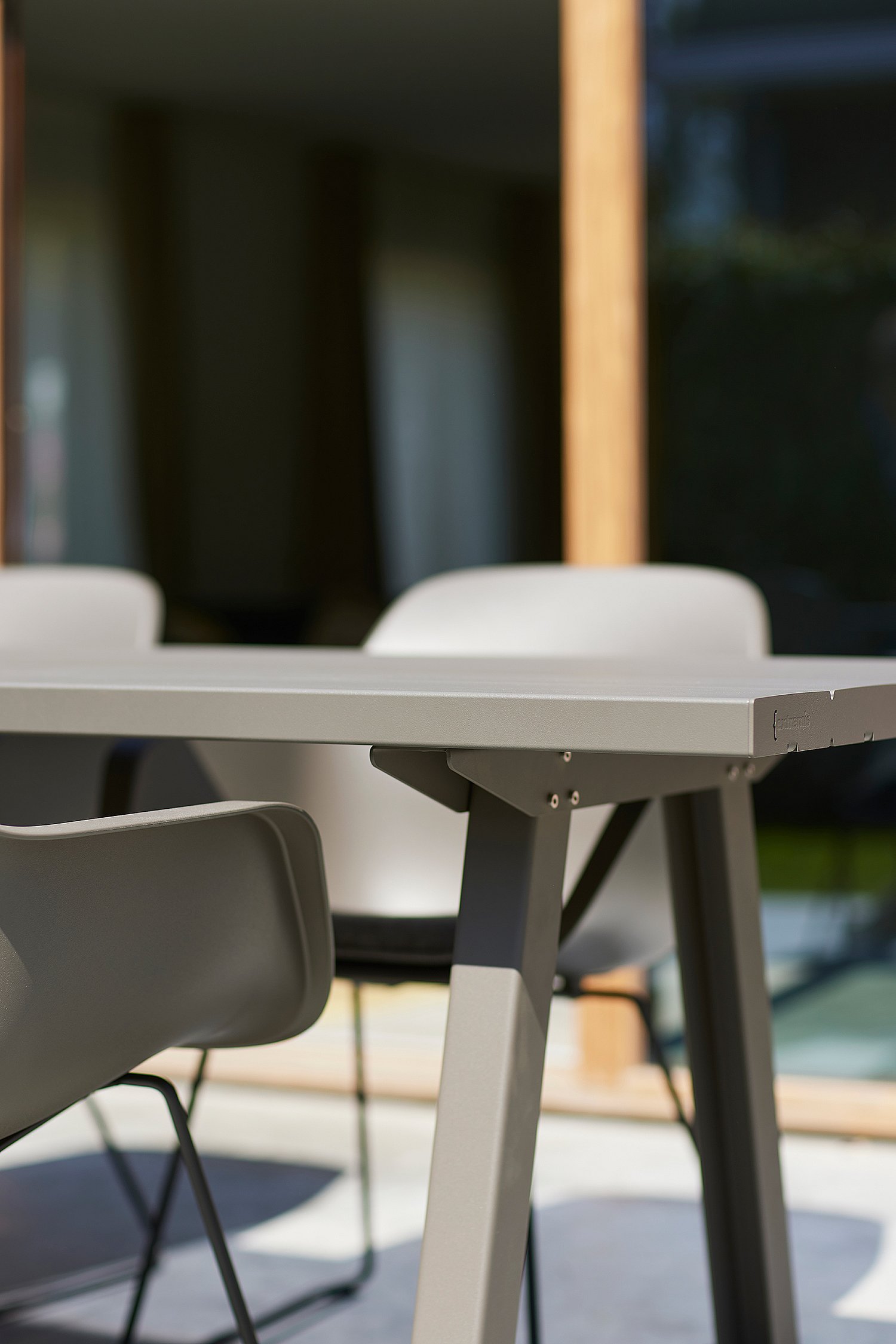 Detail of the edge and leg of a grey outdoor table, with matching chairs softly blurred in the background