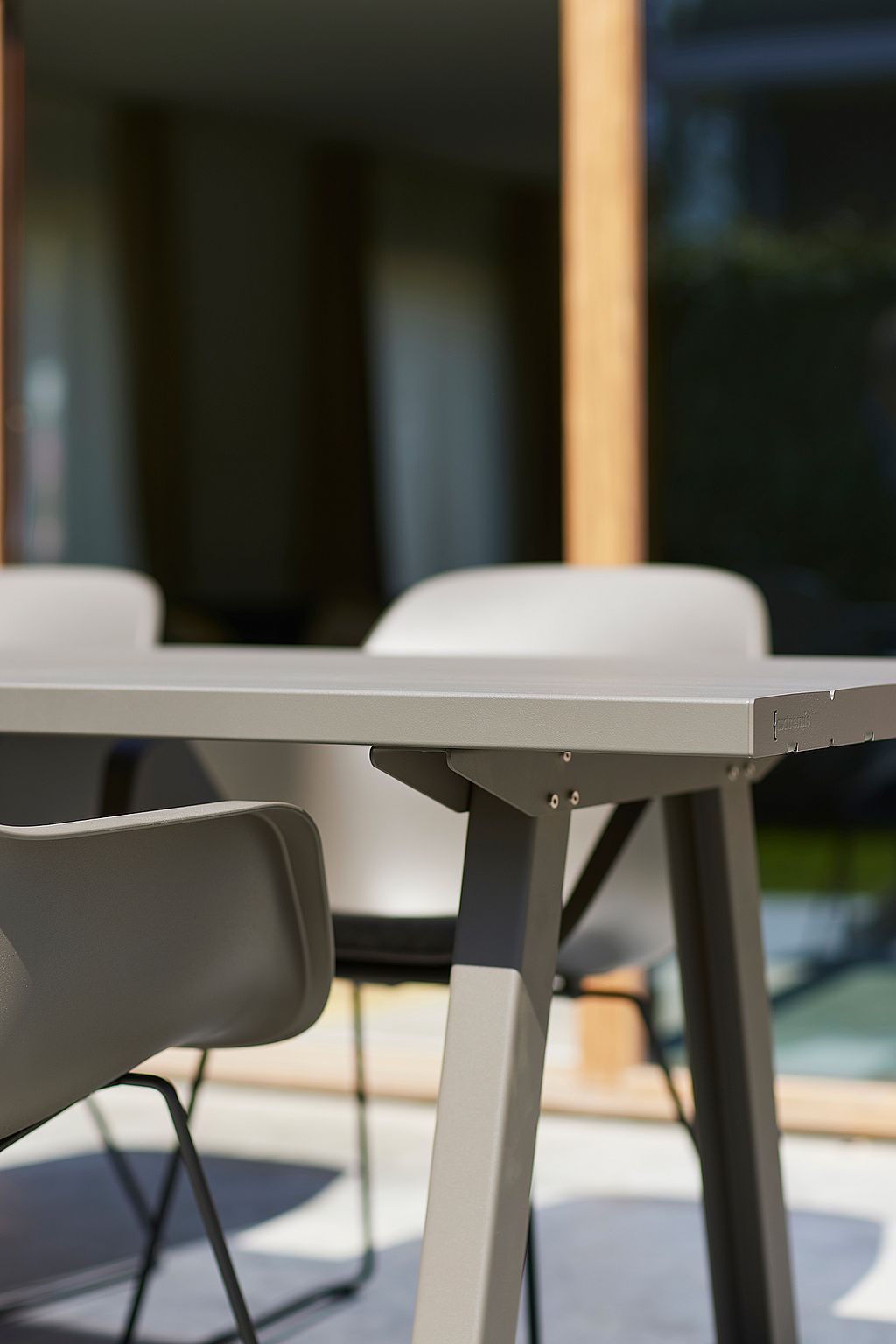Detail of the edge and leg of a grey outdoor table, with matching chairs softly blurred in the background