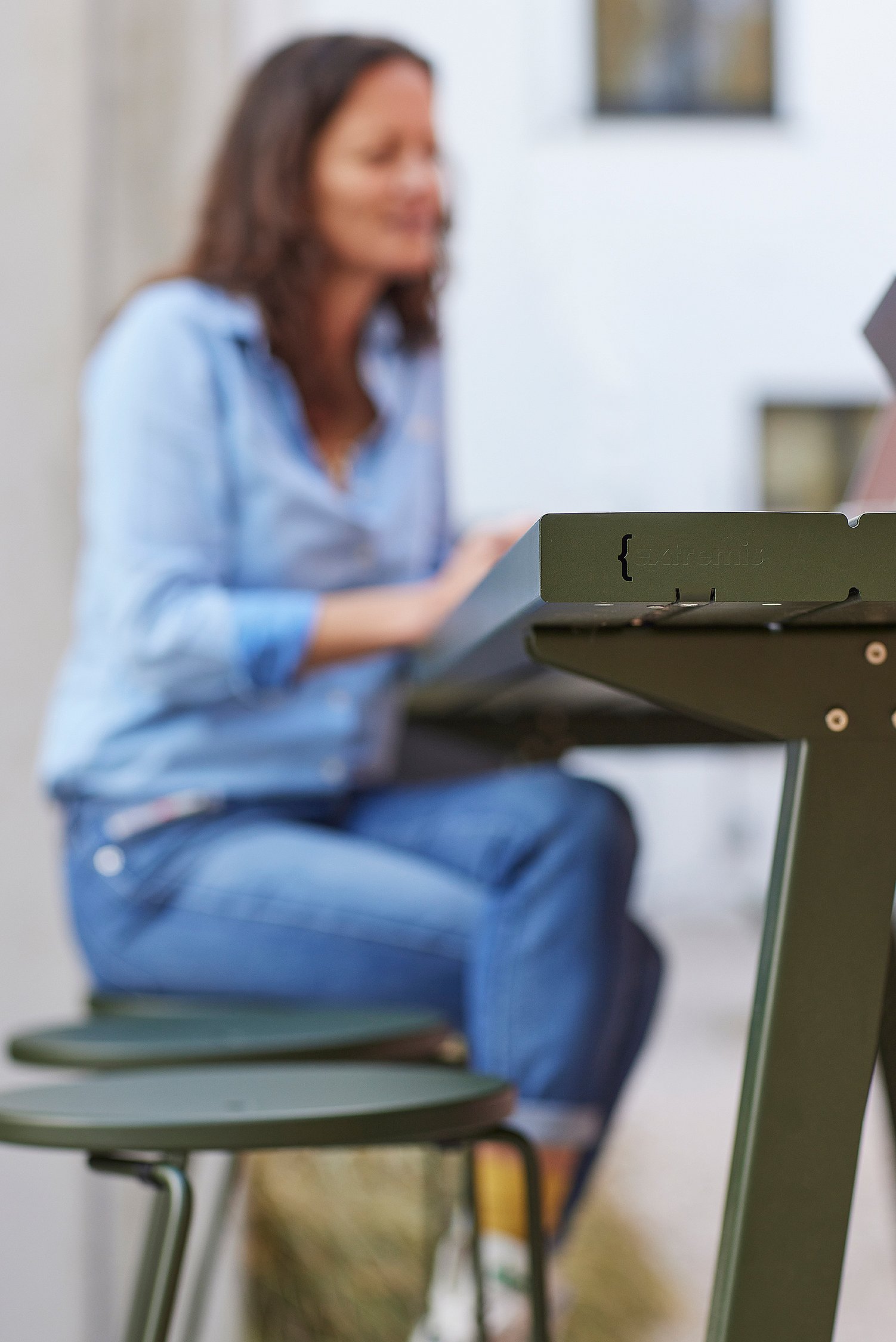 Close-up van de hoek van een op maat gemaakte Marina hoge tafel, met een vrouw die op een Tiki barkruk zit en op de achtergrond vaag in beeld is.
