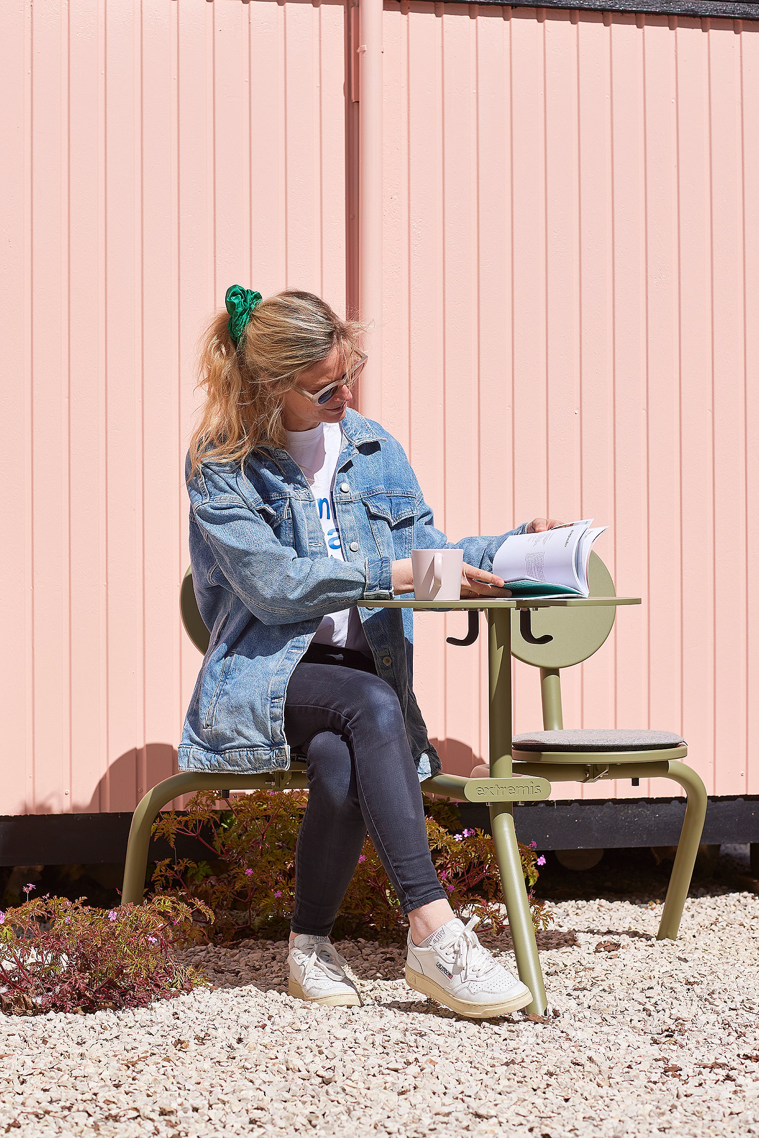 Een vrouw leest en schrijft aan een groene Bistroo tafel met vaste stoelen, geplaatst op wit grind voor een roze buitenmuur.