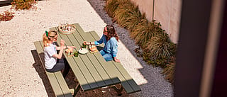 Overzicht van twee vrouwen die lunchen aan een Reed groene Marina picknicktafel op een grindterras.