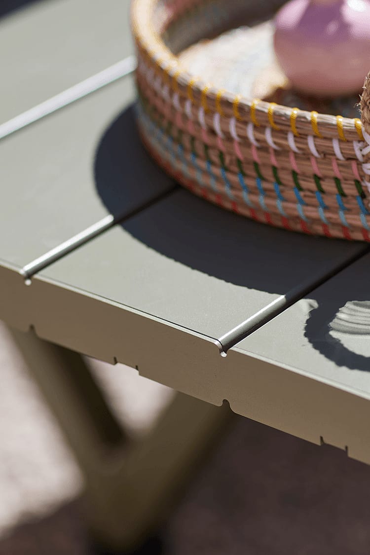Close-up van de lattenrand van een Reed groene Marina picknicktafel, met een geweven dienblad. Zonlicht.