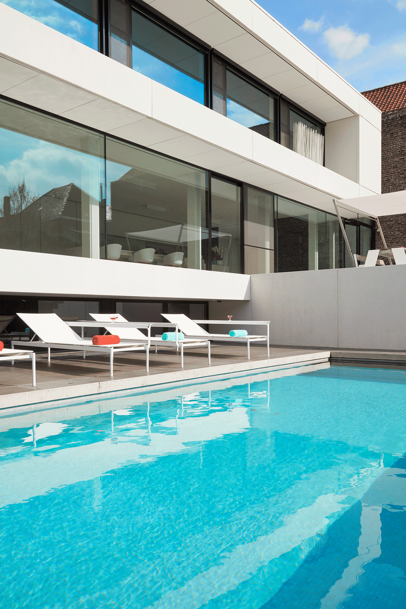 Draufsicht auf drei weiße Sol+Luna-Sofa-Sonnenliegen neben einem leuchtend blauen Pool.