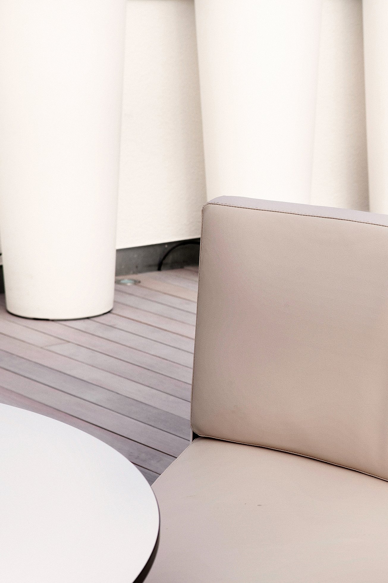Close-up of a beige seat and backrest beside a round white tabletop, with tall white cylindrical planters in the background.