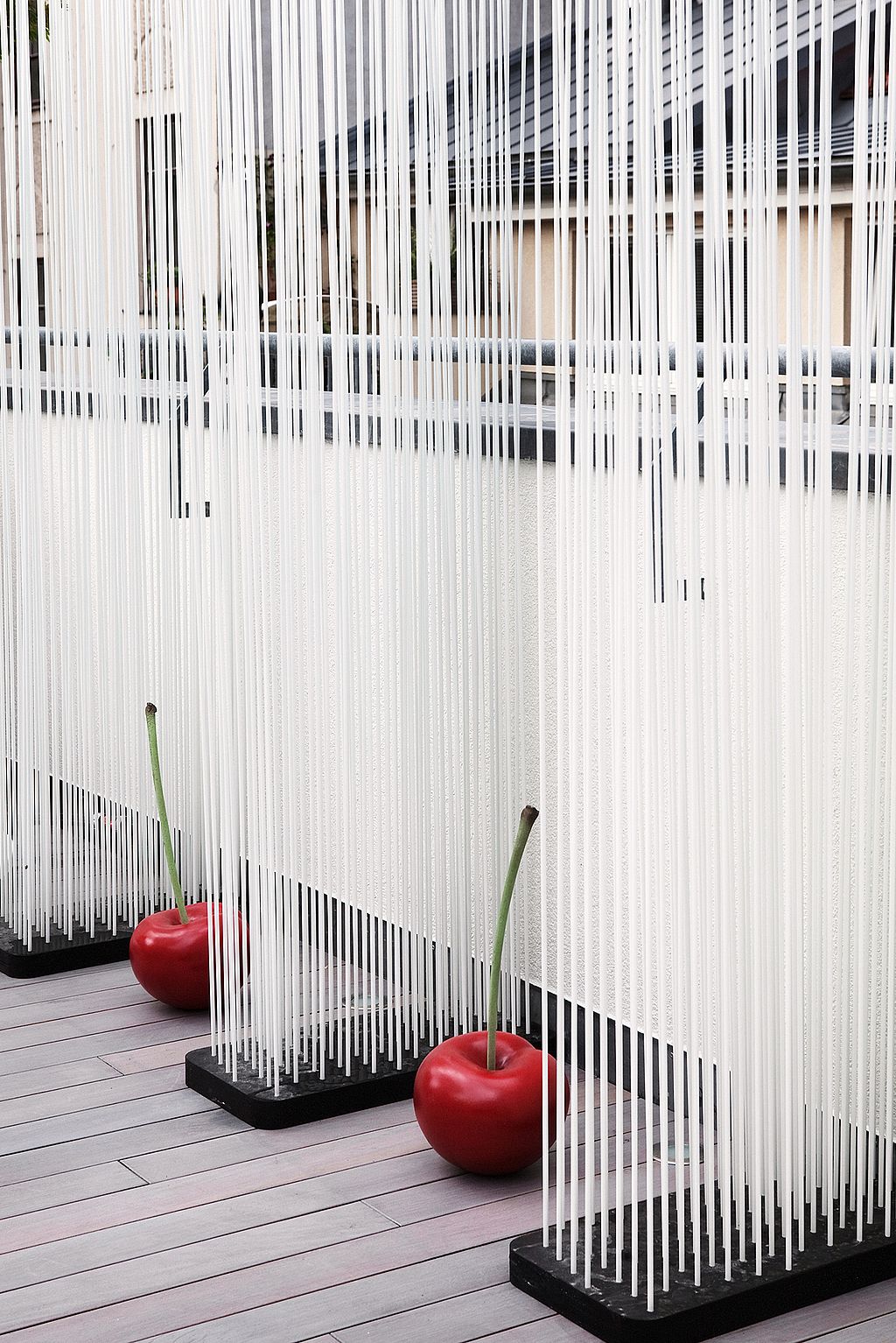 Screen made of dense vertical white rods on black bases, with two glossy red cherry ornaments placed on the timber deck in front.