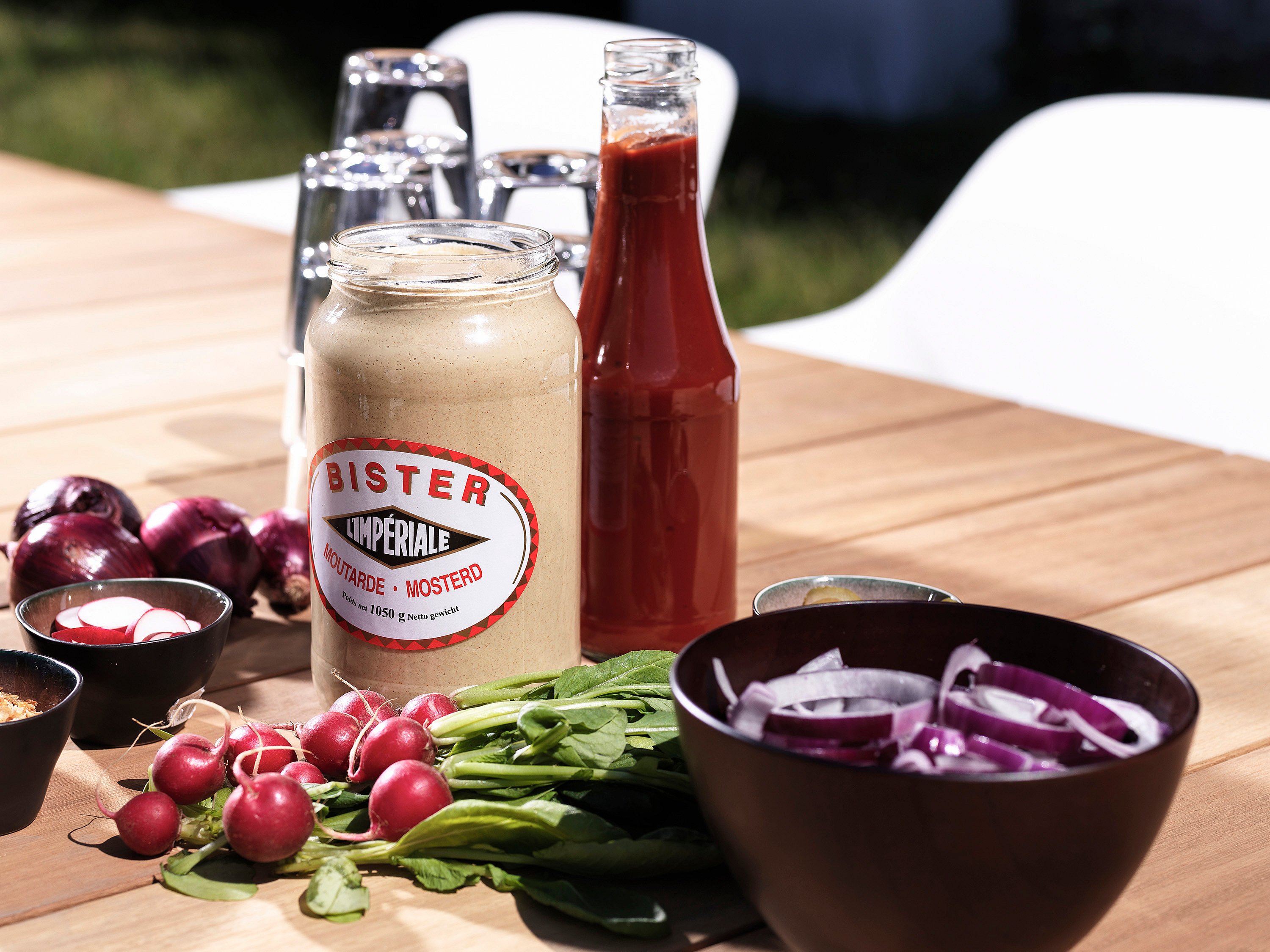 Nahaufnahme von Senf, Ketchup, geschnittenen Zwiebeln und Radieschen, angeordnet auf der Holzplatte eines Pontsūn-Tisches.