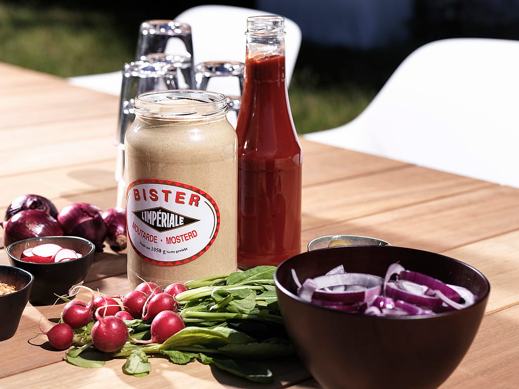 Nahaufnahme von Senf, Ketchup, geschnittenen Zwiebeln und Radieschen, angeordnet auf der Holzplatte eines Pontsūn-Tisches.