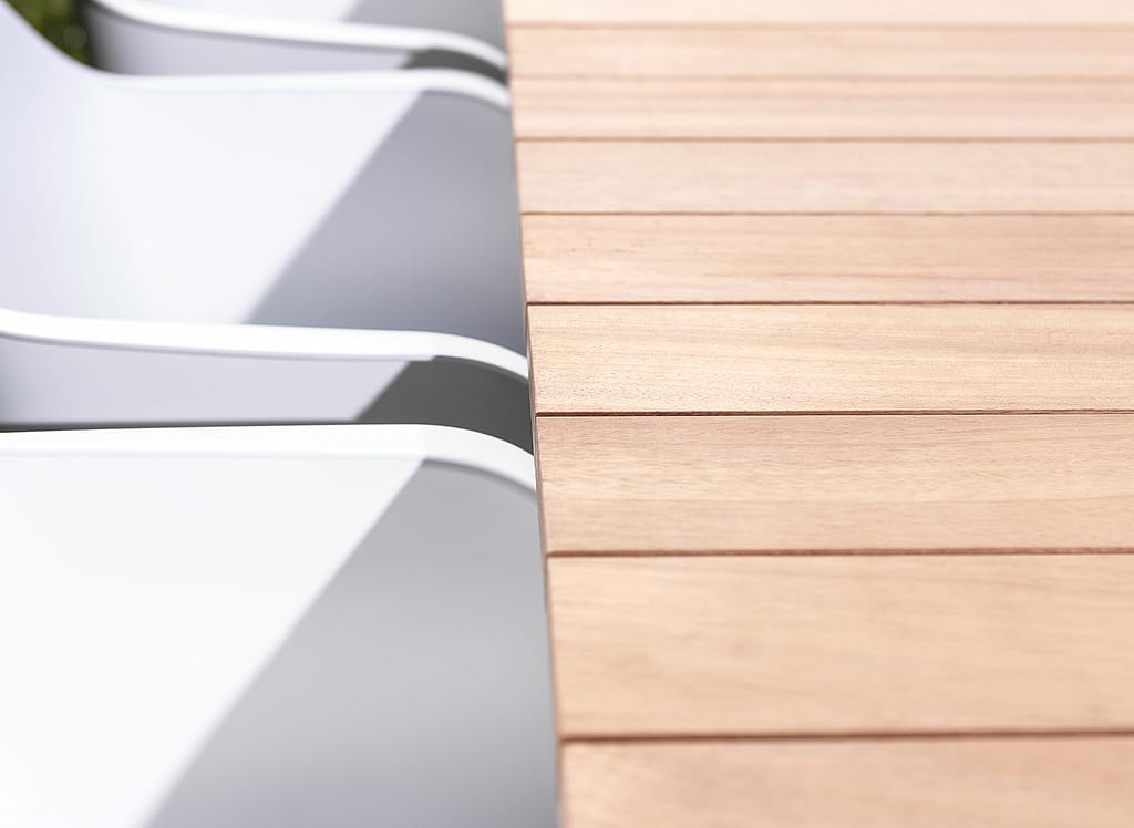 Nahaufnahme der weißen Kapitänsstühle, die neben der Holzlattenplatte eines Pontsūn-Tisches aufgereiht sind.