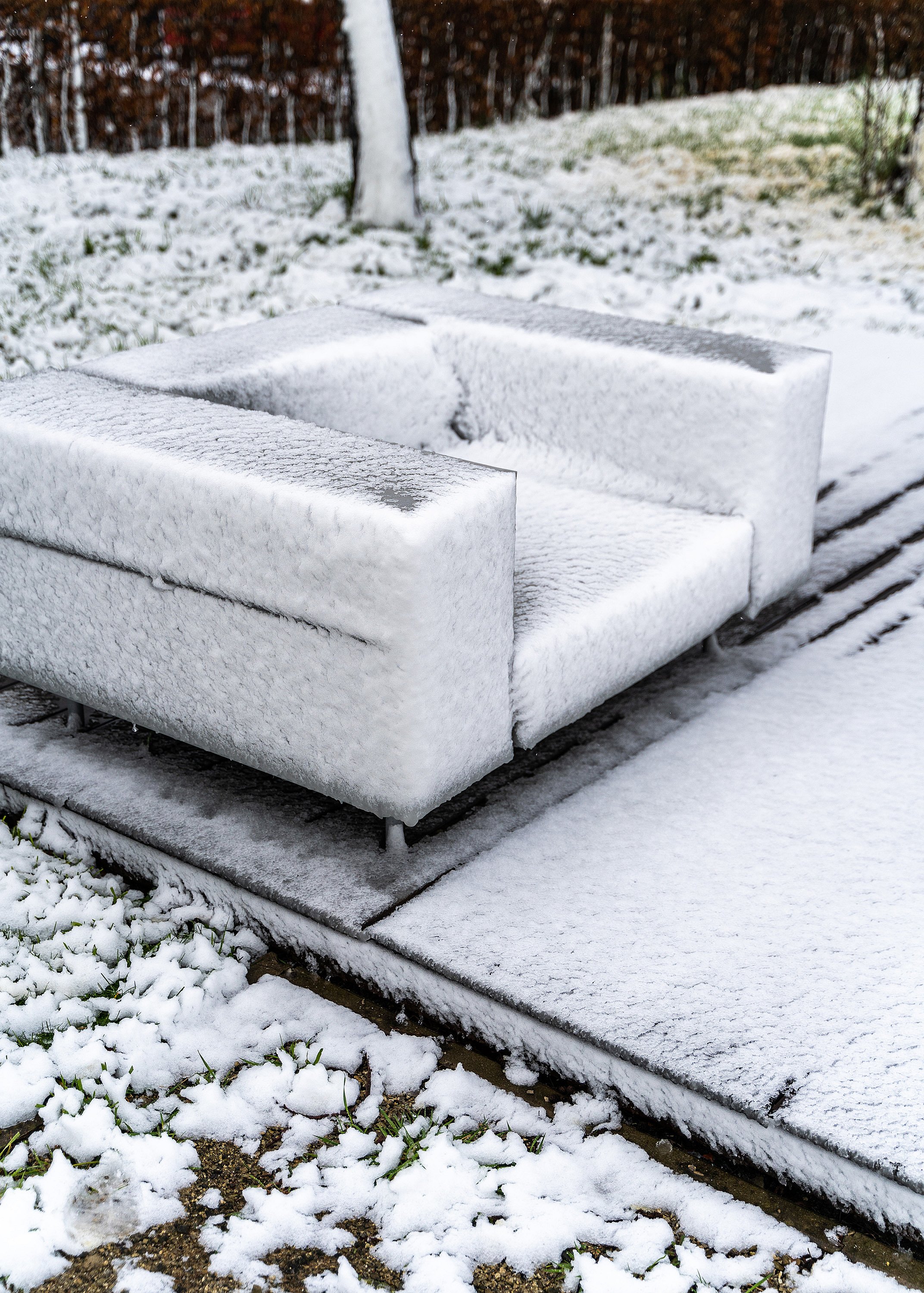 Nahaufnahme eines mit Neuschnee beschichteten Walrus-Außensofas, das auf einer Terrasse neben einem verschneiten Rasen steht.