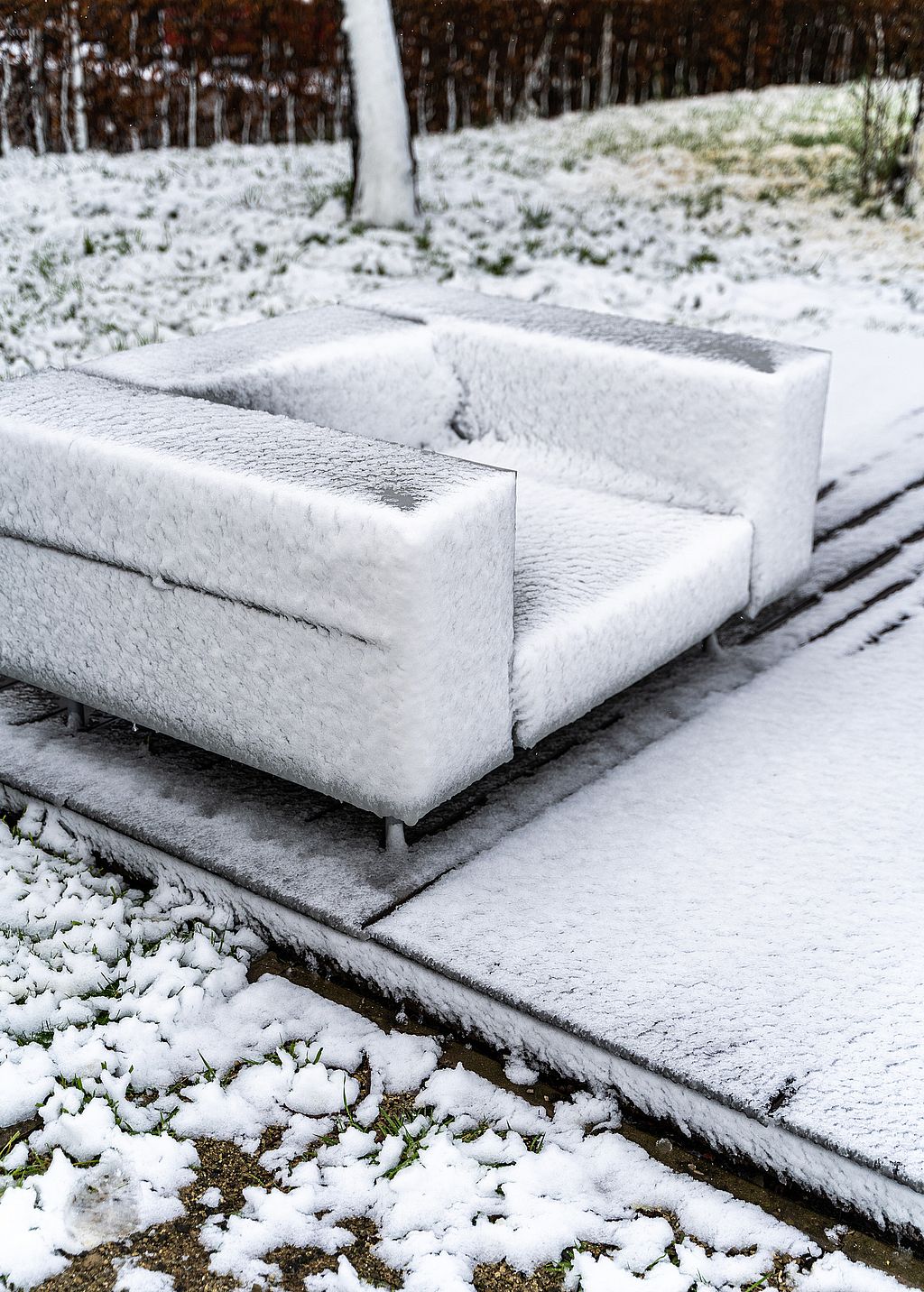 Nahaufnahme eines mit Neuschnee beschichteten Walrus-Außensofas, das auf einer Terrasse neben einem verschneiten Rasen steht.