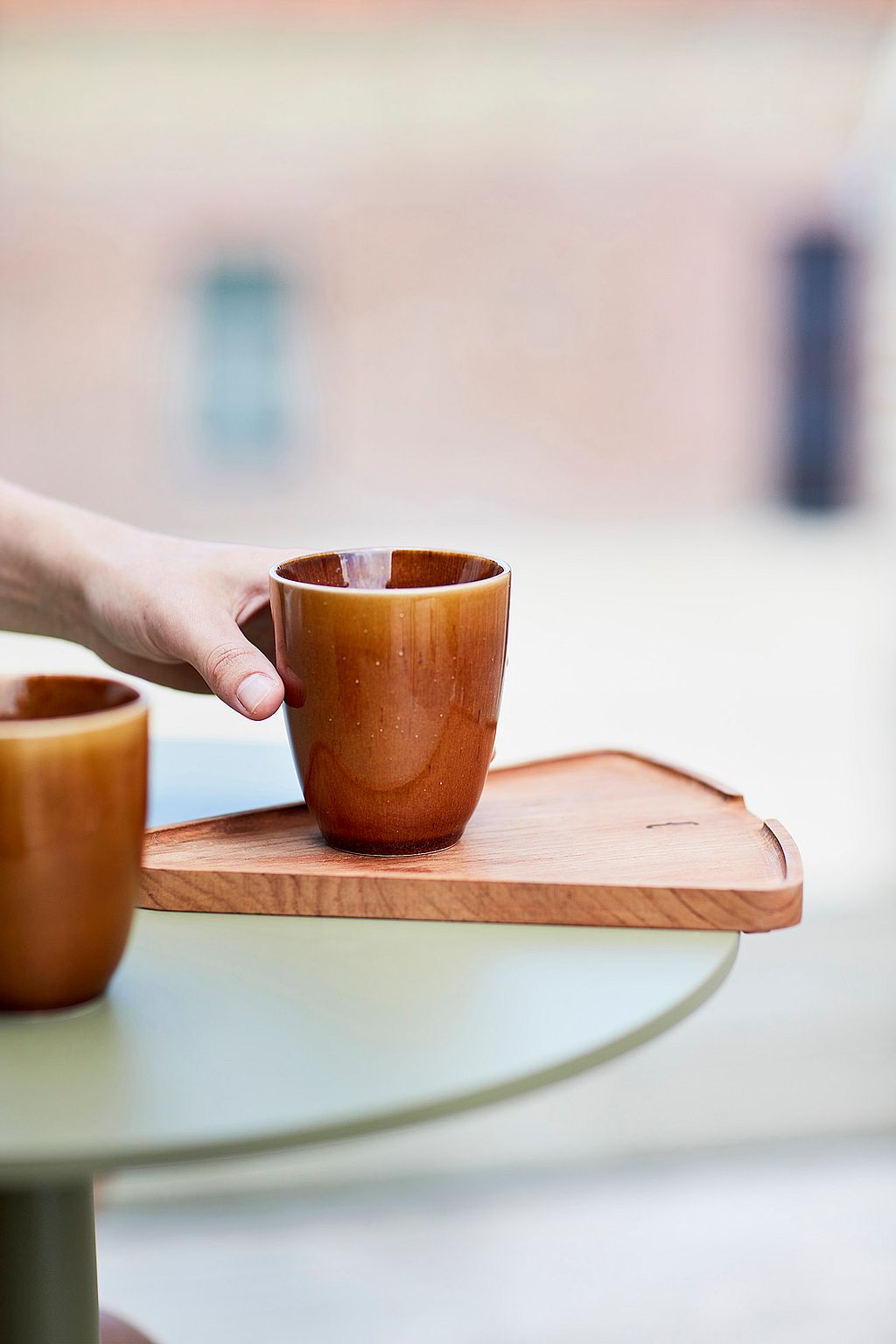 Een hand plaatst een bruine kop op het houten verlengstuk van een rietgroene Bistroo-tafel.