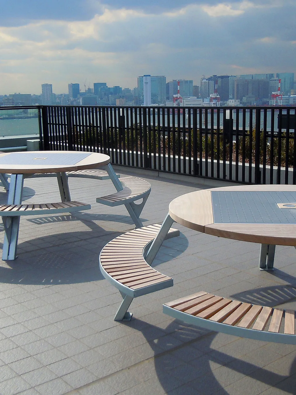 Three Gargantua picnic tables stand on a rooftop terrace overlooking Tokyo’s waterfront skyline under a dramatic cloudy sky.