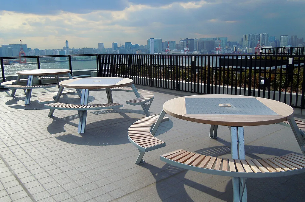 Drei Gargantua-Picknicktische stehen auf einer Dachterrasse mit Blick auf die Skyline der Tokyo Waterfront unter einem spektakulären bewölkten Himmel.