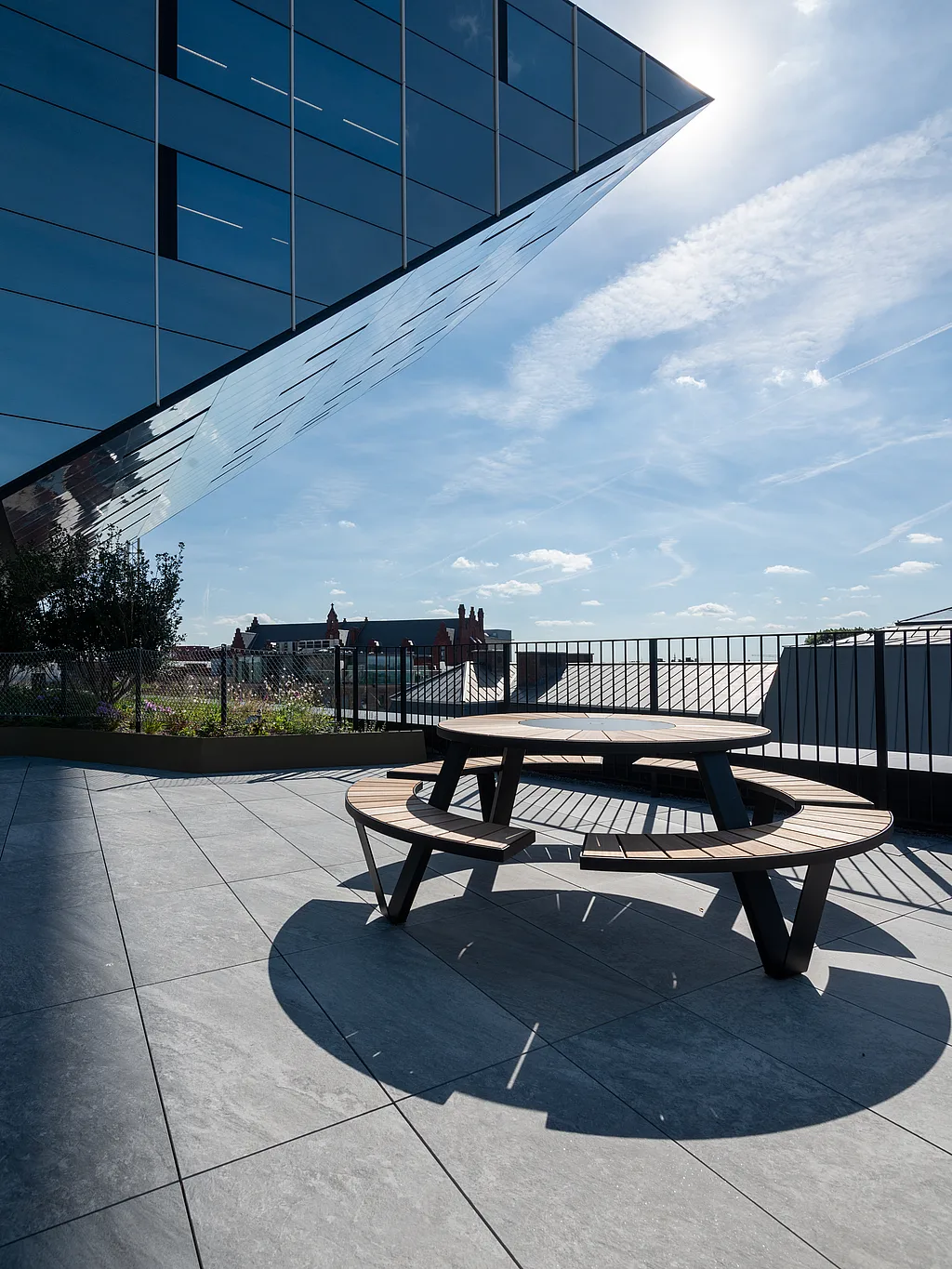 A Pantagruel picnic table stands on the rooftop terrace beneath the dramatic mirrored overhang of Hasselt’s city hall, with the skyline and planting visible in the background.
