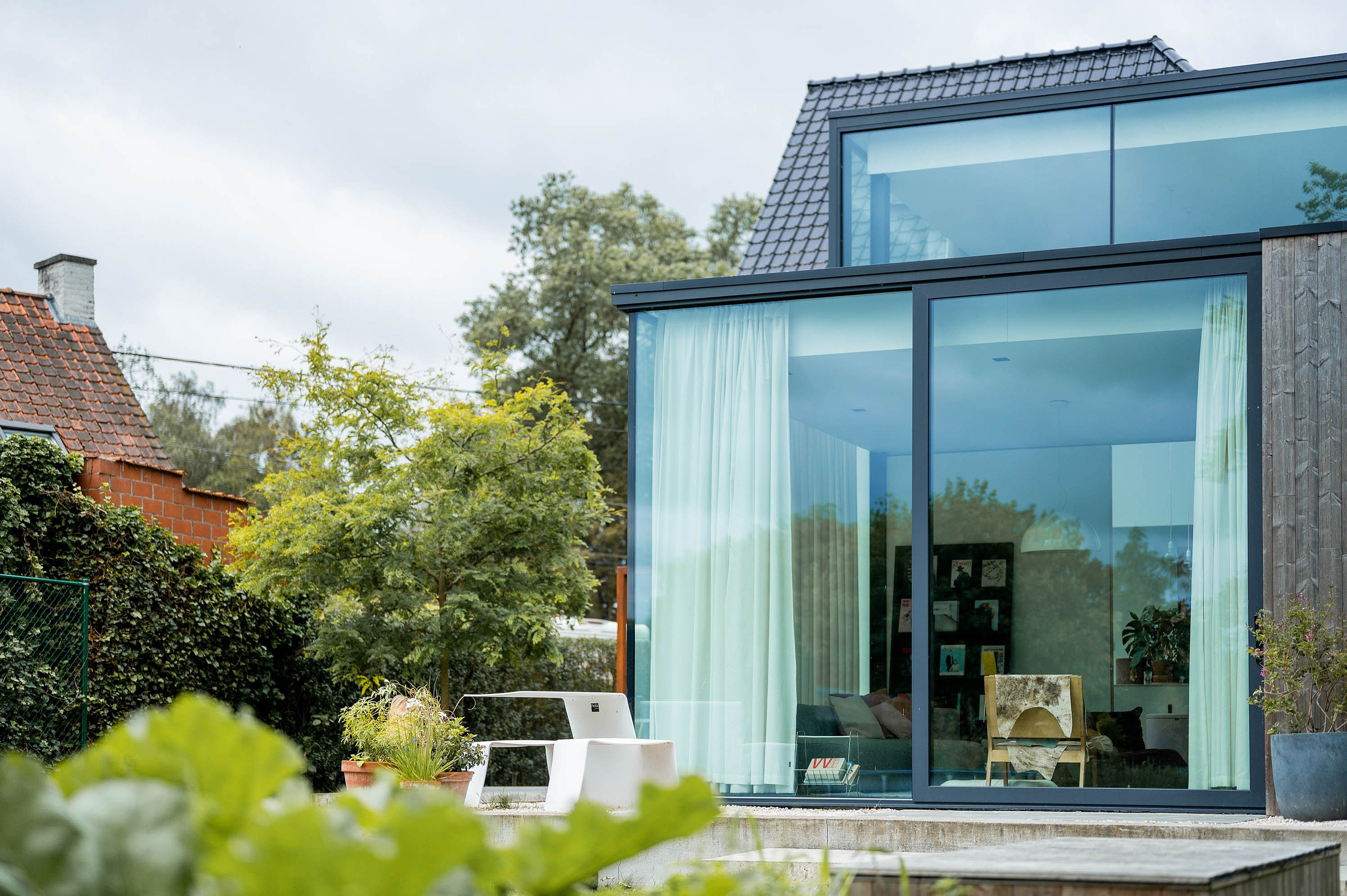 A white Picnik table sits beside the floor-to-ceiling windows of a contemporary house, with vegetable leaves and the garden softly framing the scene.
