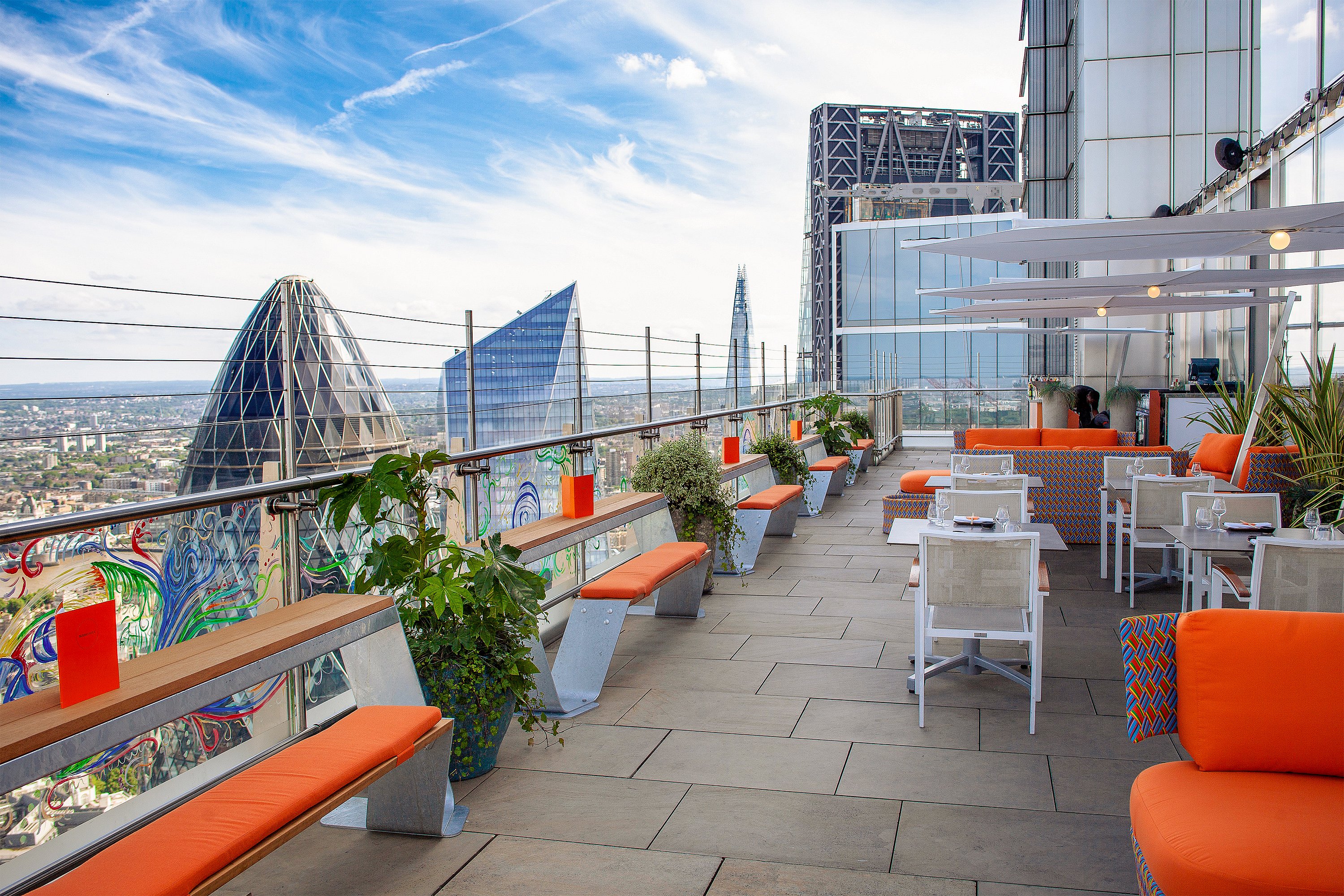 Dachterrasse mit orange gepolsterten Hopper-Bänken und farbenfrohen Lounge-Sitzgelegenheiten mit Blick auf die Skyline von London und freiem Blick auf den Gherkin.