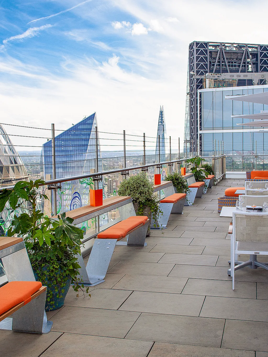 Dachterrasse mit orange gepolsterten Hopper-Bänken und farbenfrohen Lounge-Sitzgelegenheiten mit Blick auf die Skyline von London und freiem Blick auf den Gherkin.