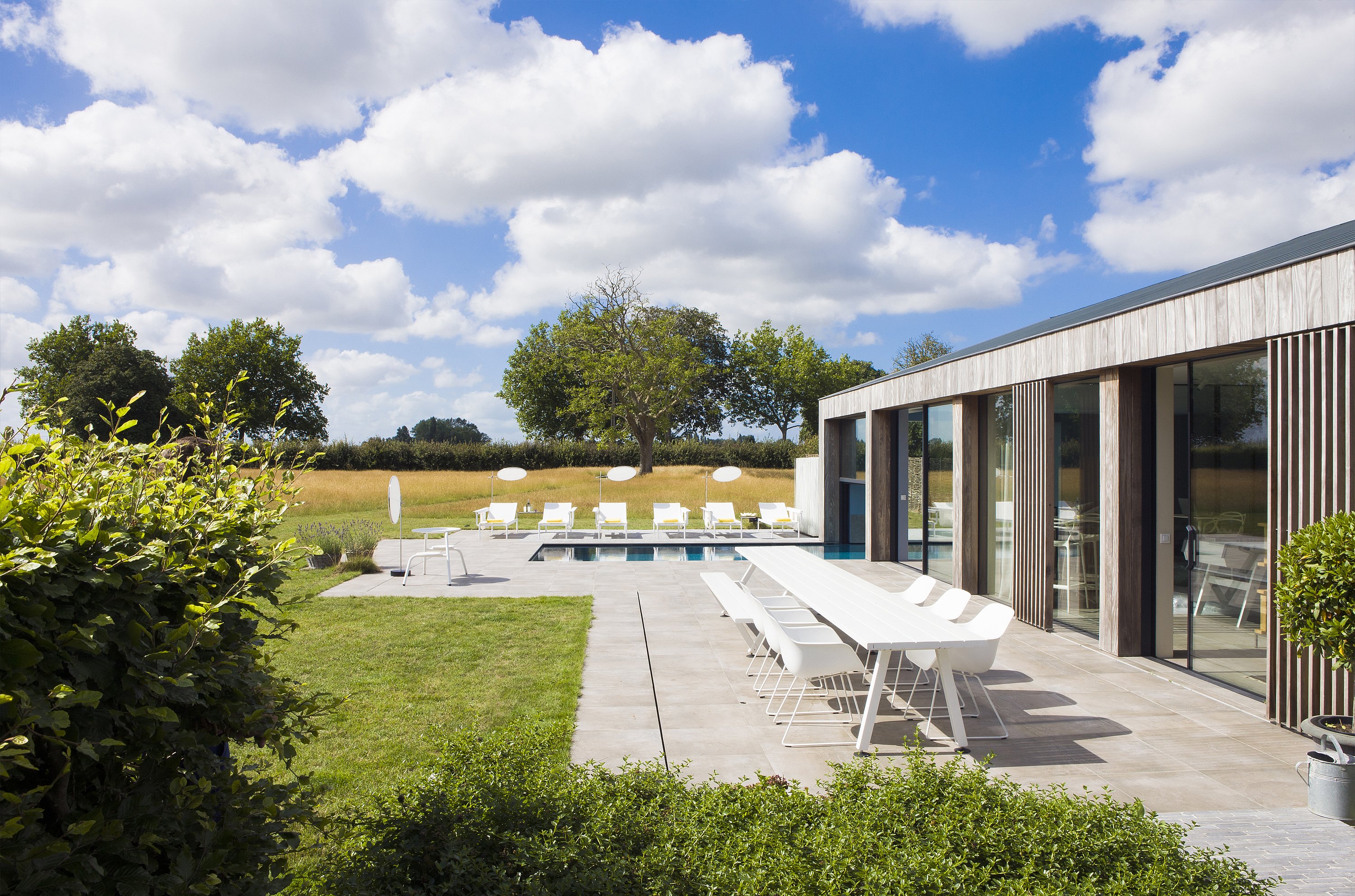 Large vue sur la maison de vacances moderne avec un combo Marina blanc et des chaises assorties sur la terrasse, tandis que les chaises longues blanches Sol+Luna sont assises au bord de la piscine en arrière-plan.