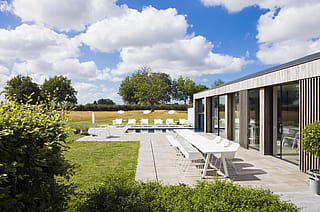 Large vue sur la maison de vacances moderne avec un combo Marina blanc et des chaises assorties sur la terrasse, tandis que les chaises longues blanches Sol+Luna sont assises au bord de la piscine en arrière-plan.