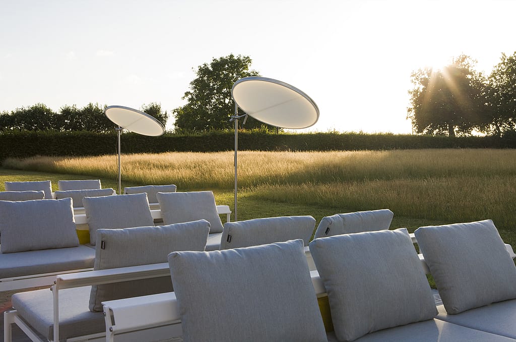 Gros plan de coussins arrière pâles sur des chaises longues blanches Sol+Luna, avec le soleil du soir bas brillant à travers la prairie au-delà.
