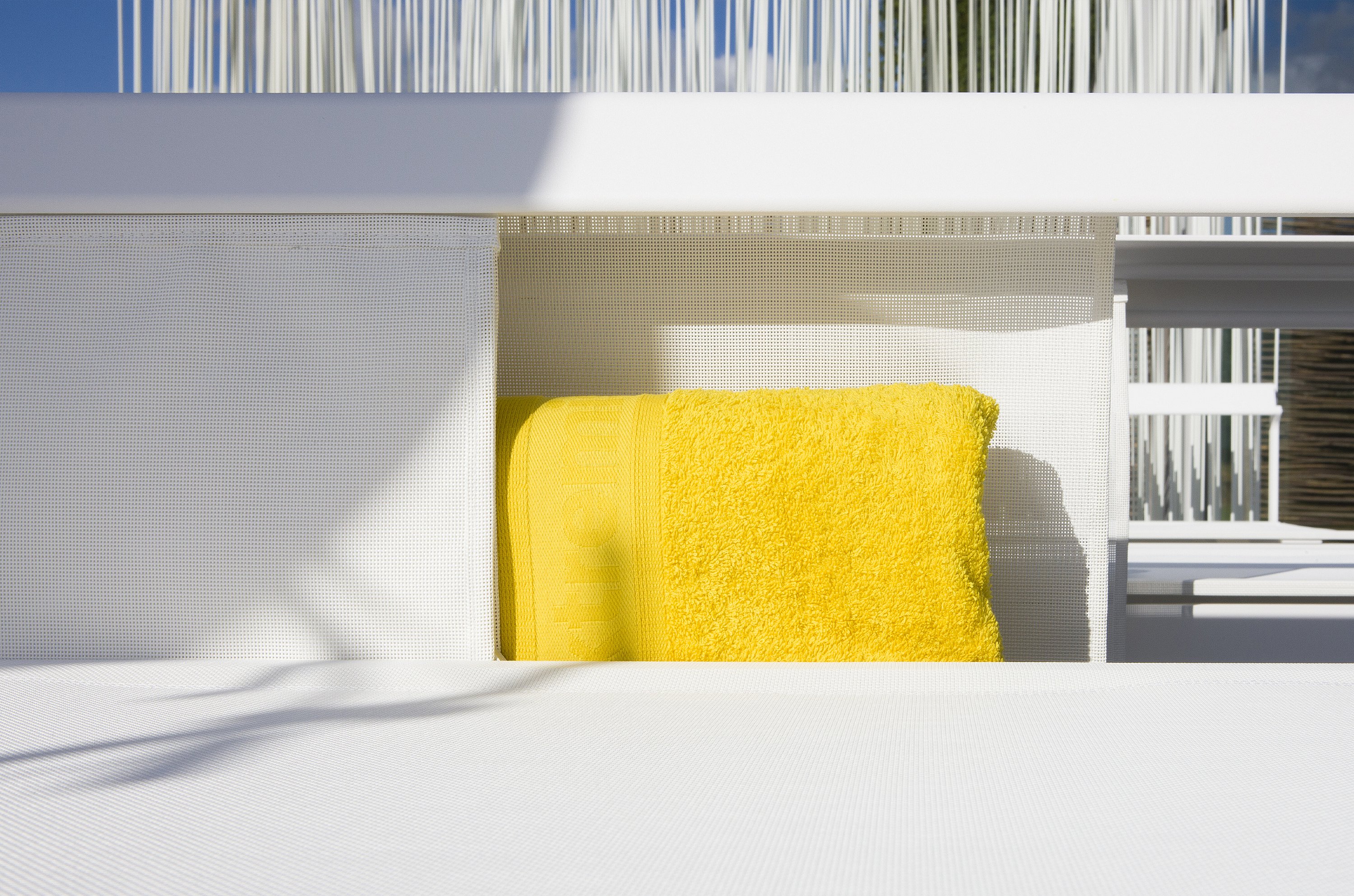 Détail d’un transat Sol+Luna blanc avec une serviette jaune rentrée dans le compartiment de rangement intégré derrière le siège.