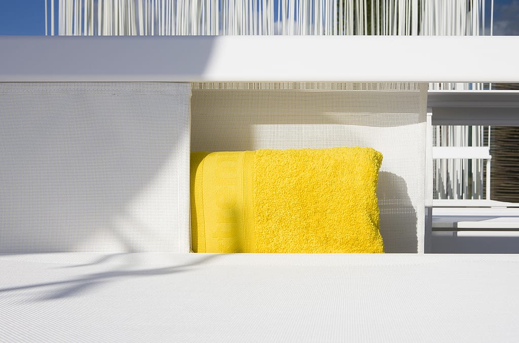 Détail d’un transat Sol+Luna blanc avec une serviette jaune rentrée dans le compartiment de rangement intégré derrière le siège.