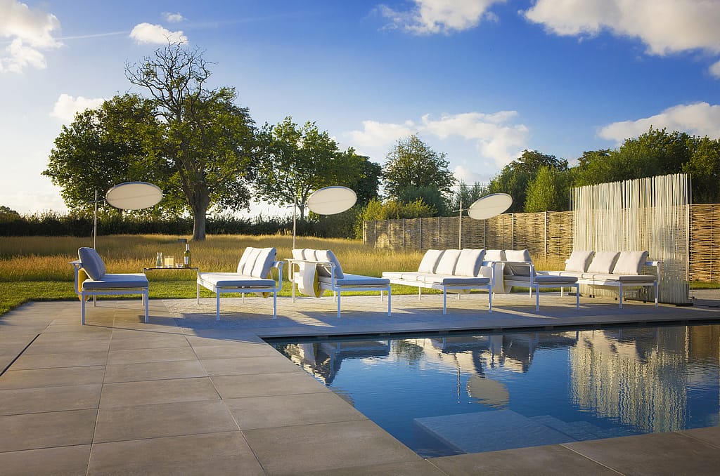 À l’heure dorée, des chaises longues blanches Sol+Luna avec des coussins pâles entourent la piscine, créant un cadre de salon en plein air détendu sous le soleil du soir.