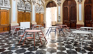 Wide view of the historic chapel classroom showing multiple coloured Virus tables arranged across the glossy checkerboard floor beneath richly decorated walls and tall wooden doors.