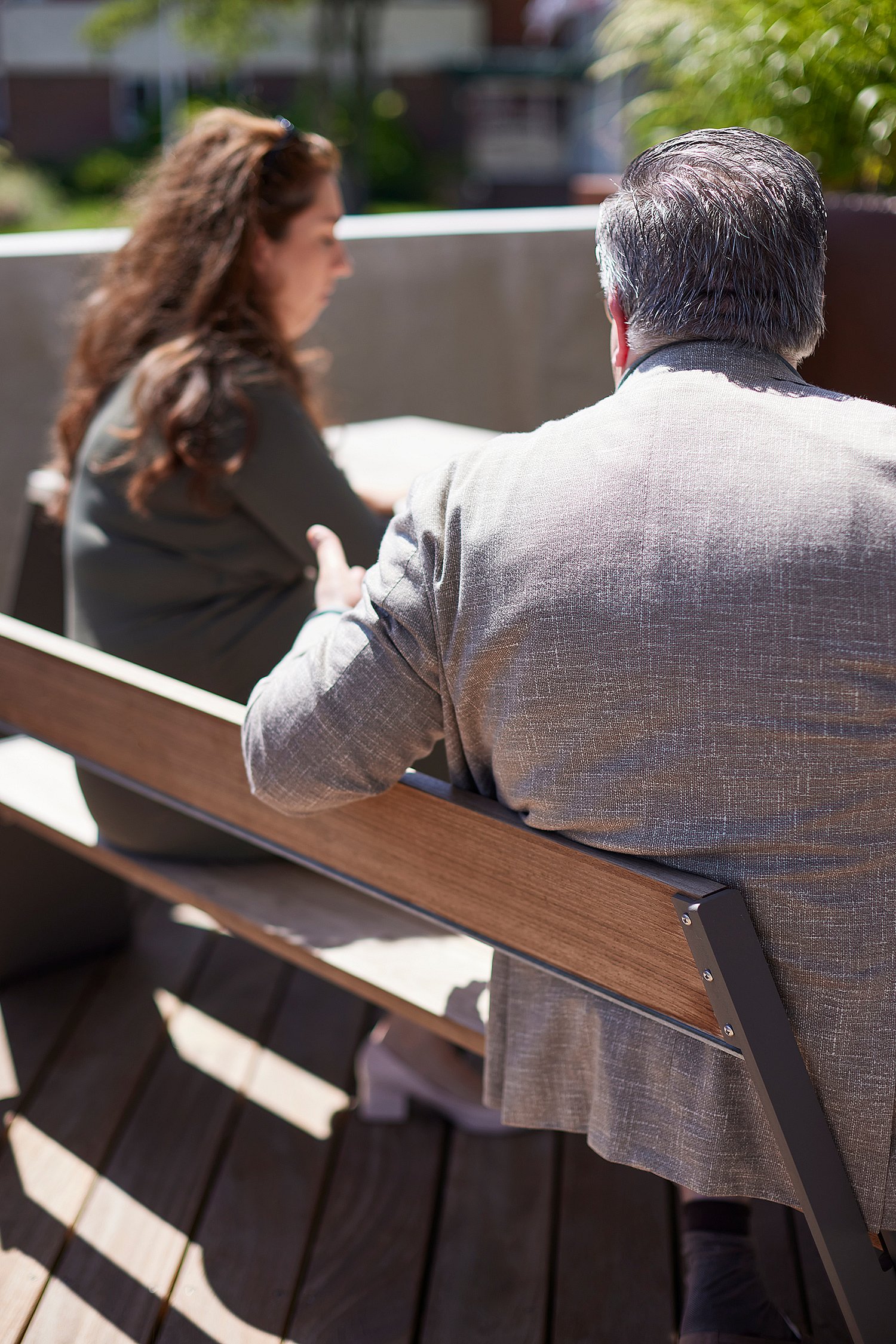 Gros plan par derrière de deux personnes assises sur le banc du dossier d’une table de pique-nique Hopper lors d’une conversation sur la terrasse.