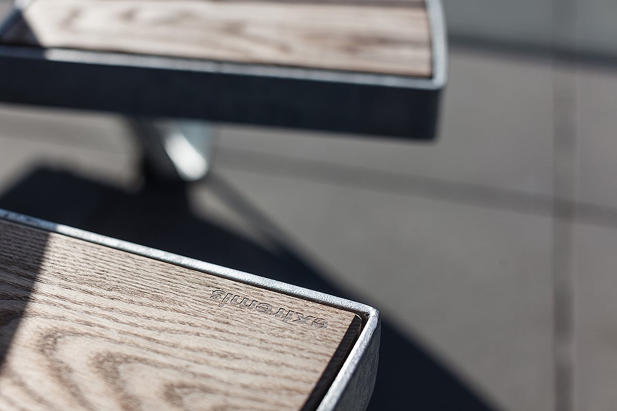 Close-up van houten tafelhoeken met het Extremis-logo gegraveerd, omlijst door gegalvaniseerde metalen randen en zachte schaduwen.