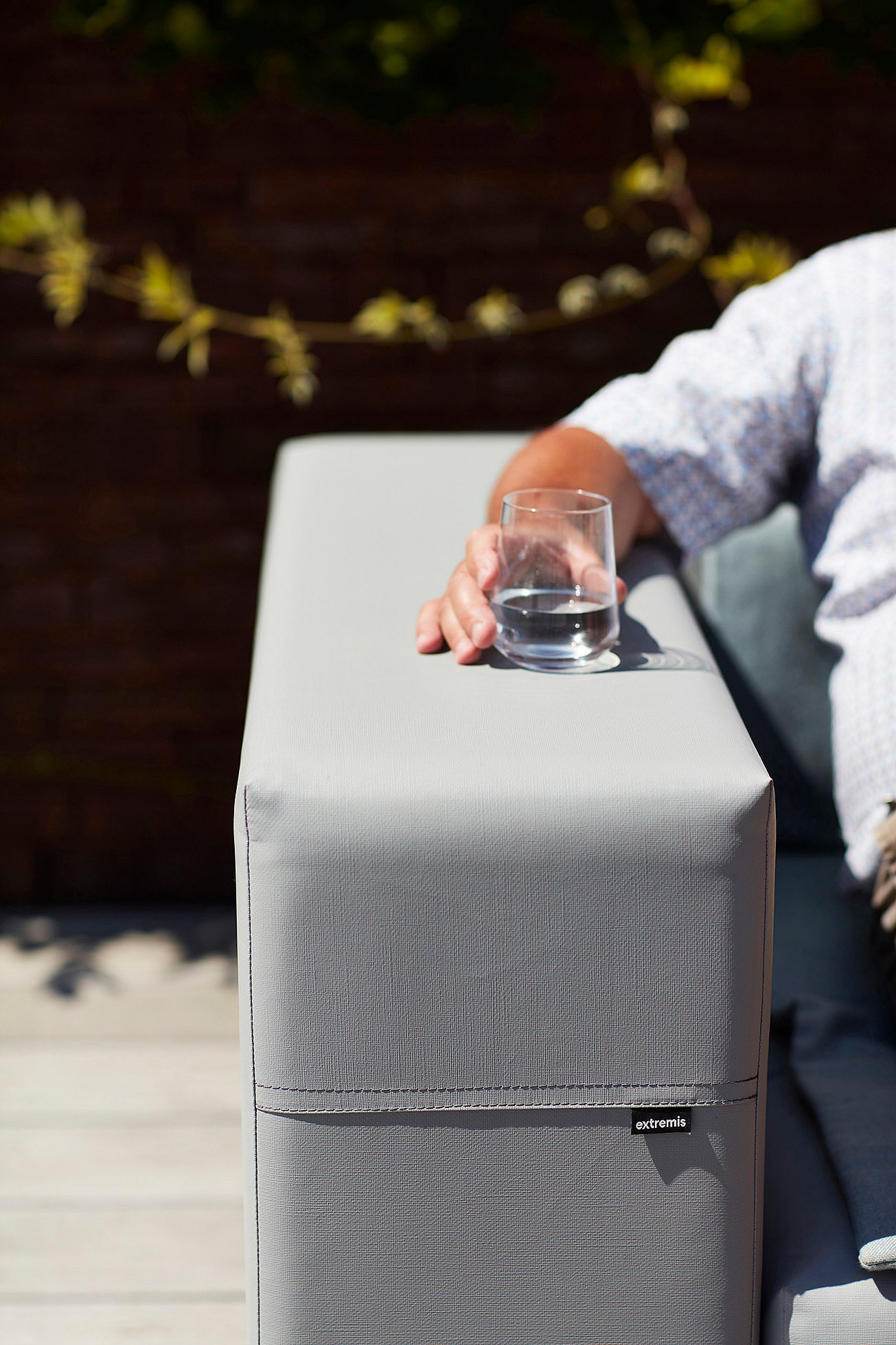 Close-up of the armrest of a light grey Walrus sofa with a tumbler of water resting on top.