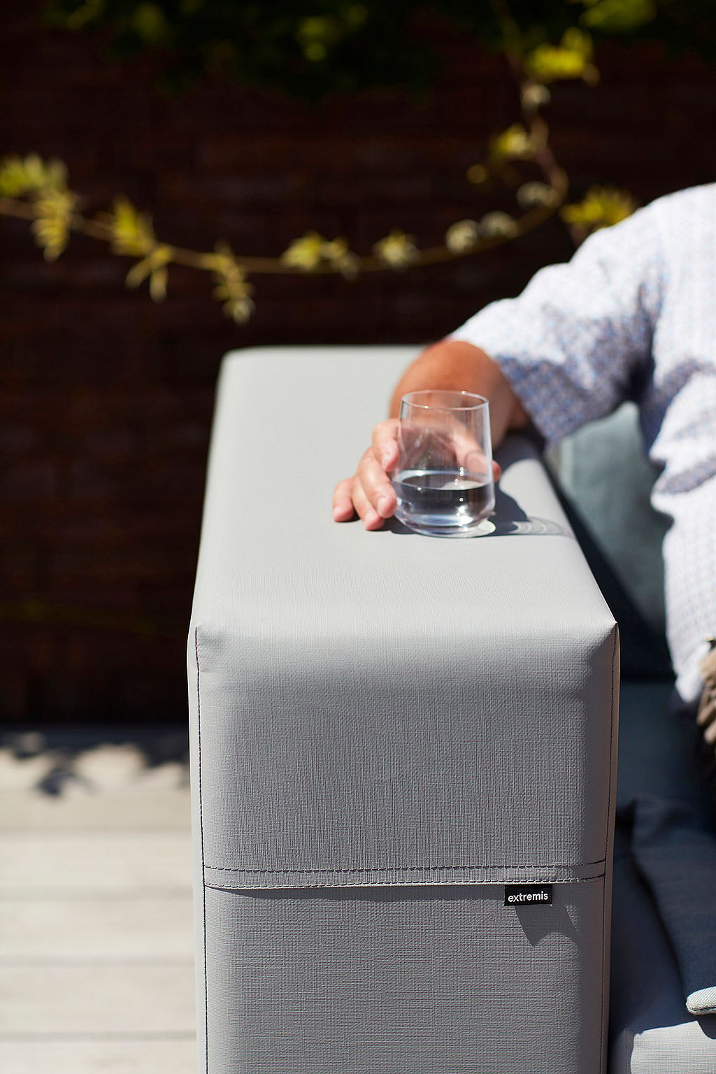 Close-up of the armrest of a light grey Walrus sofa with a tumbler of water resting on top.