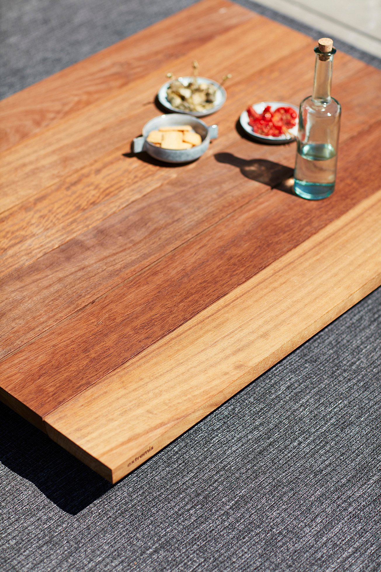 Close-up of the low wooden coffee table on a dark outdoor rug, styled with a glass bottle and small dishes.