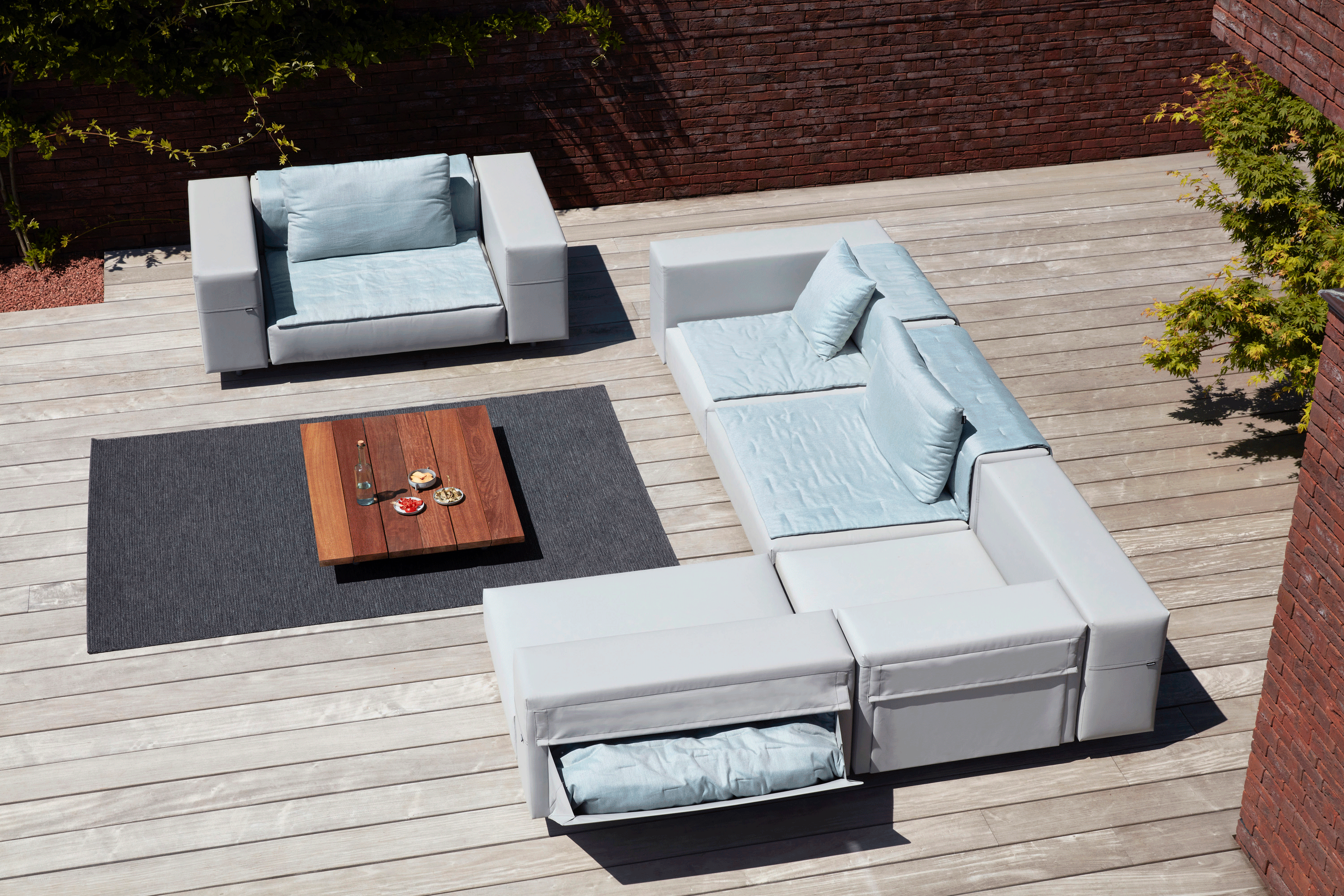Luftaufnahme eines grauen, modularen Walrus-Sofas und Sessels mit hellblauen Kissen auf einer Holzterrasse.