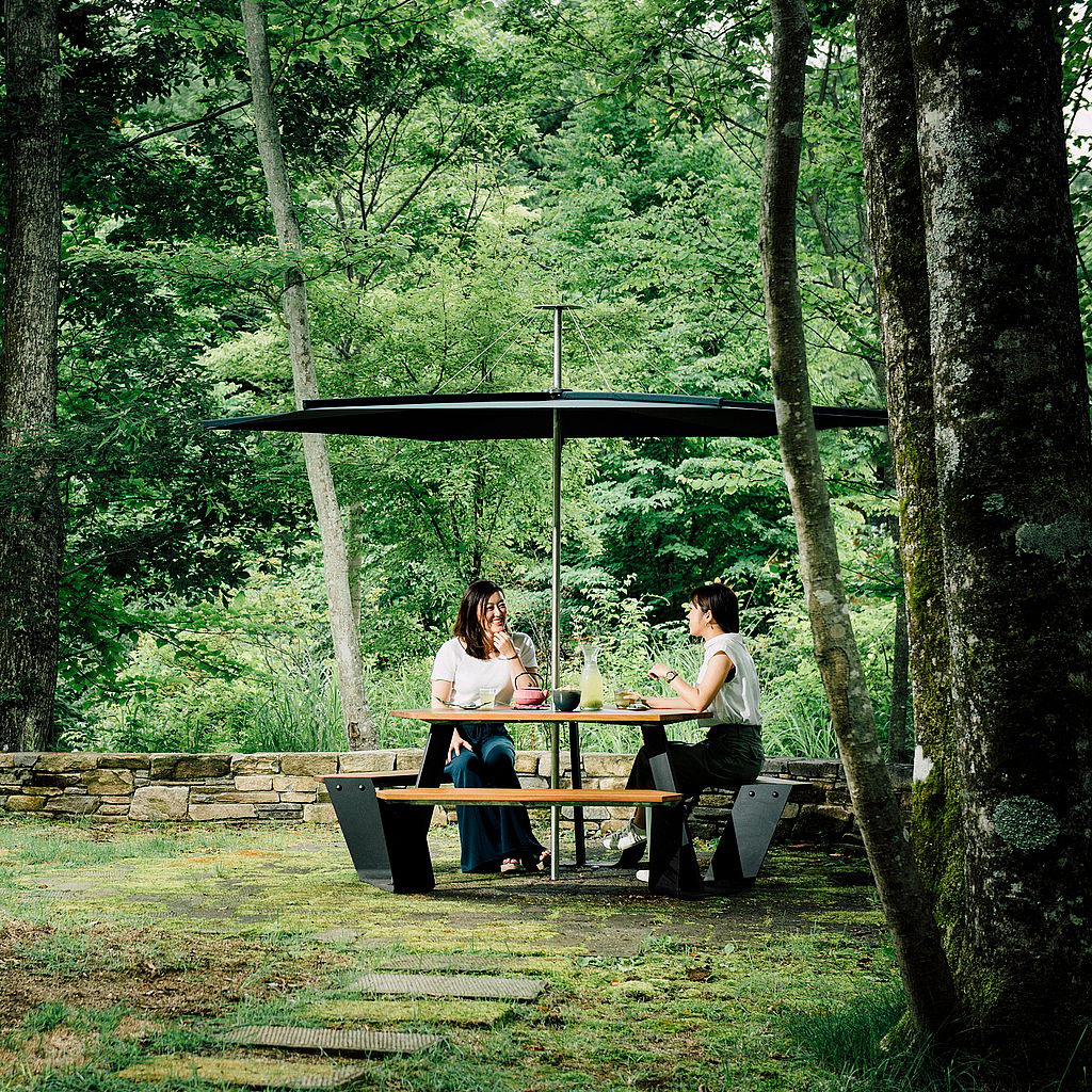Two people sitting at a black Anker picnic table with canopy in a wooded garden.