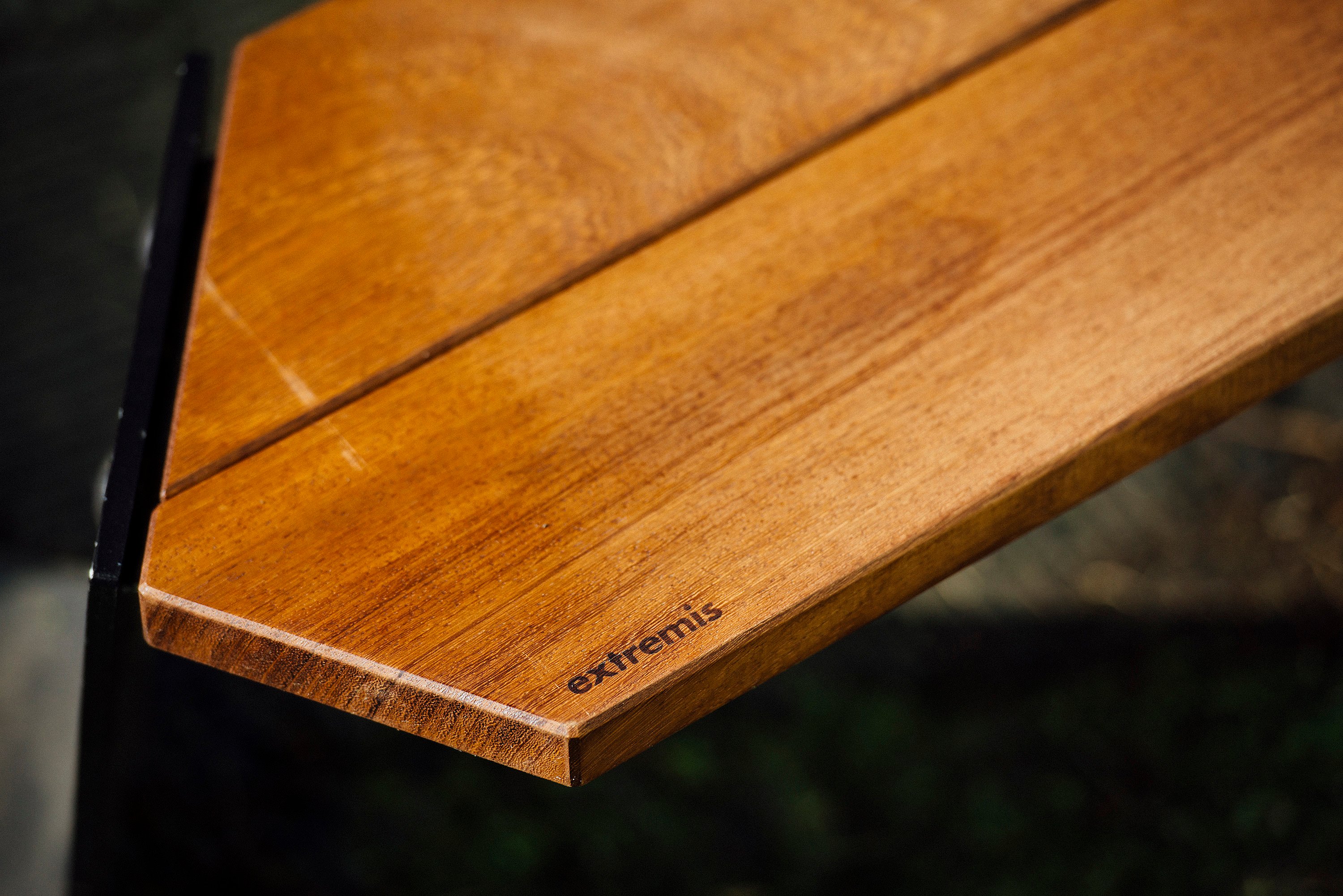 Close-up of a warm-toned wooden tabletop corner with the Extremis logo engraved near the edge.