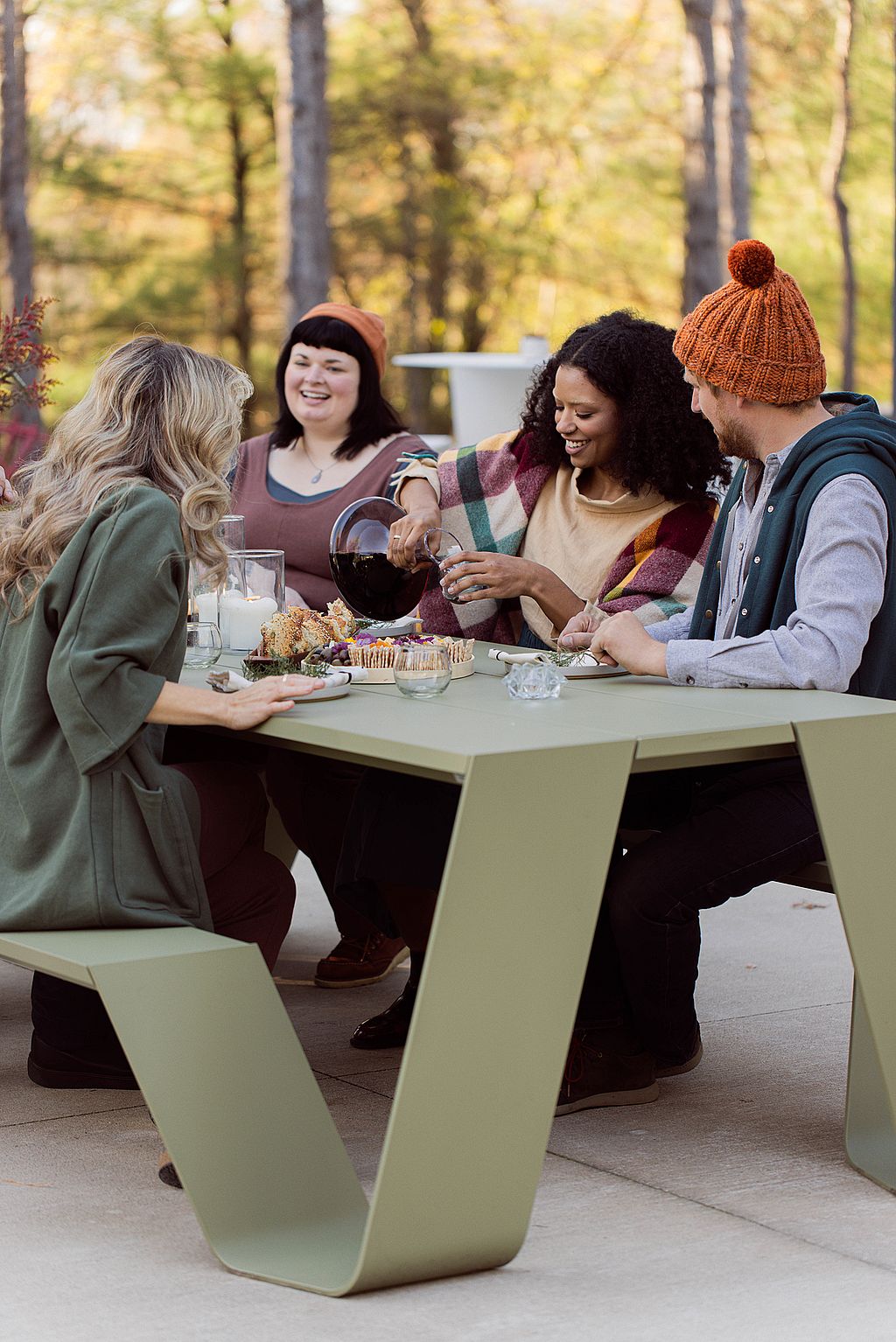 Vier vrienden zaten buiten rond een groene Picnik-tafel, schonken een warm drankje en praatten over kaarsen en snacks.